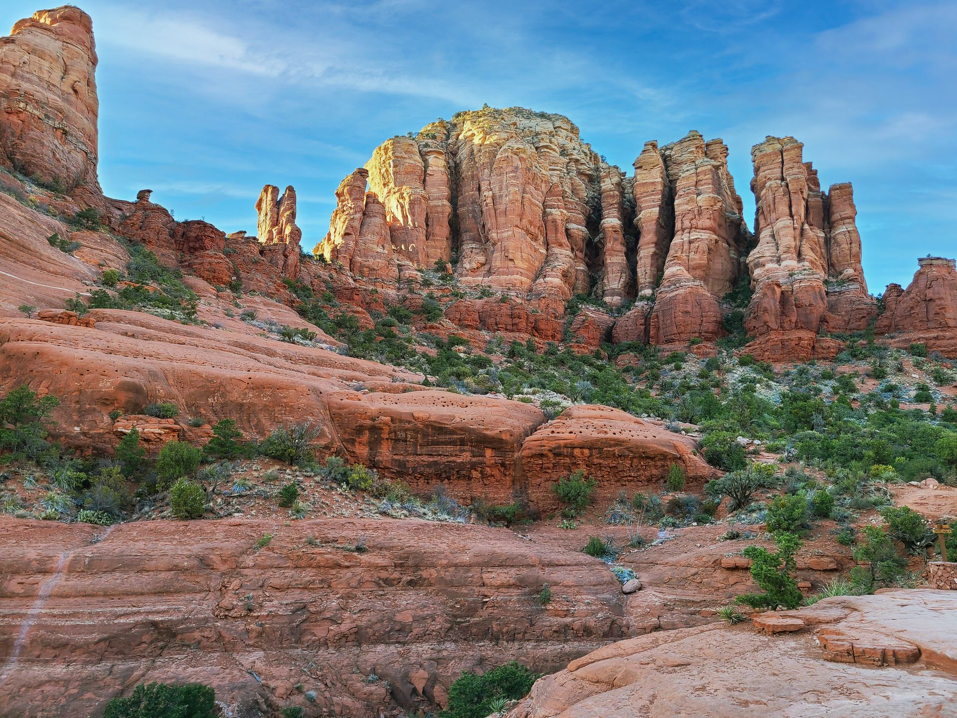 An orange rock face with white stripes throughout the rocks. There are green trees scattered around the cliff.