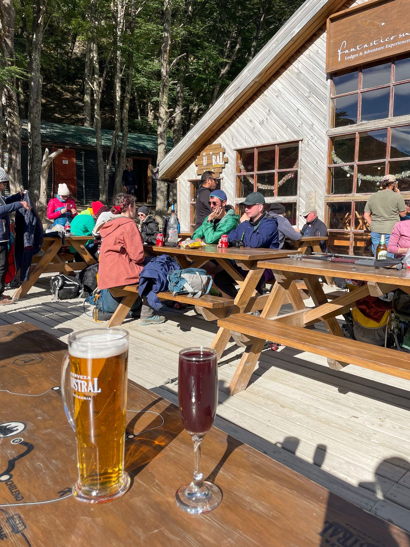 A beer and a glass with a purple drink outside on a picnic table at El Chileno. Several people sit at other tables in the background.