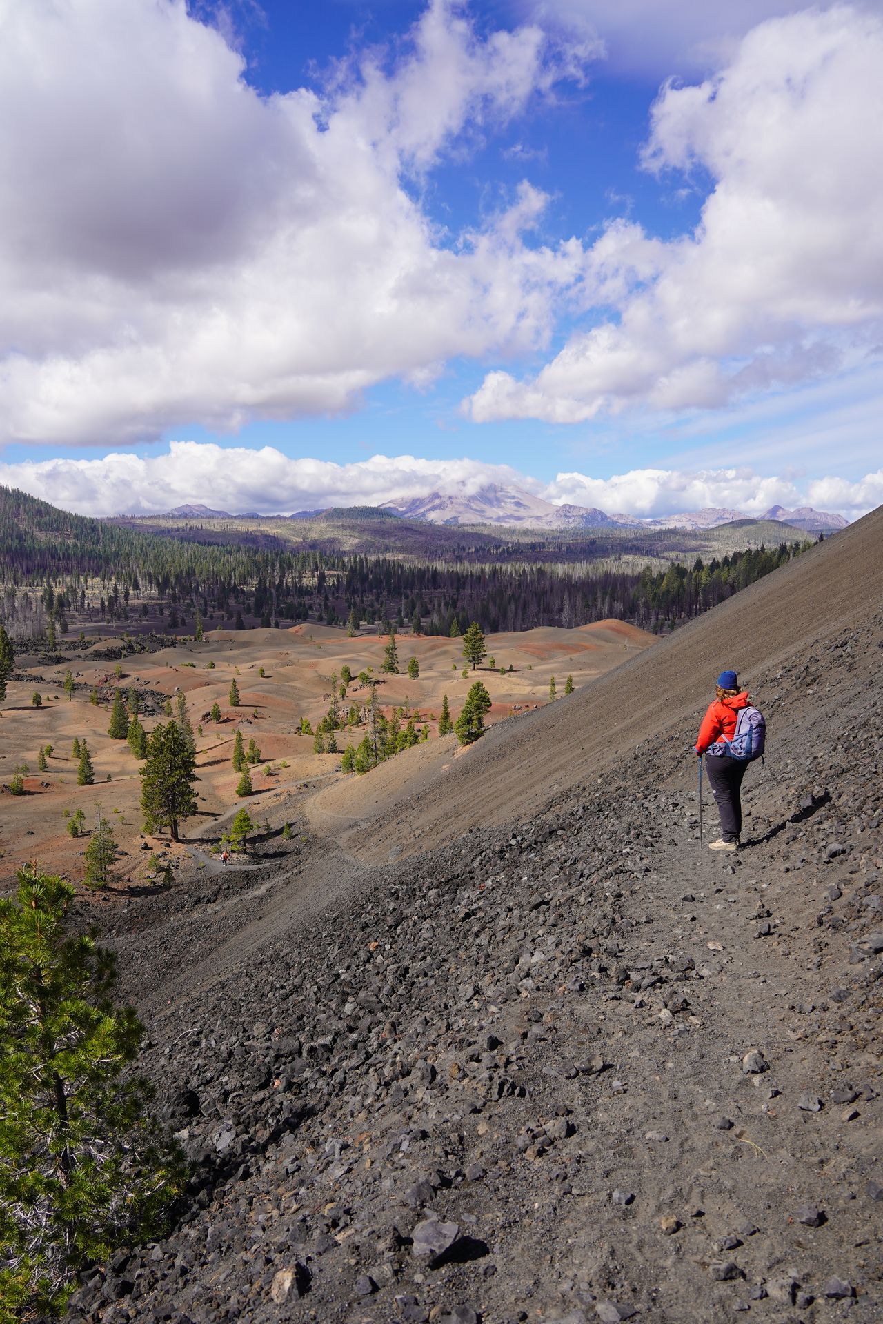 Lydia hiking down the backside of the Cinder Cone trail with views of lava dunes and Lassen Peak in the distance