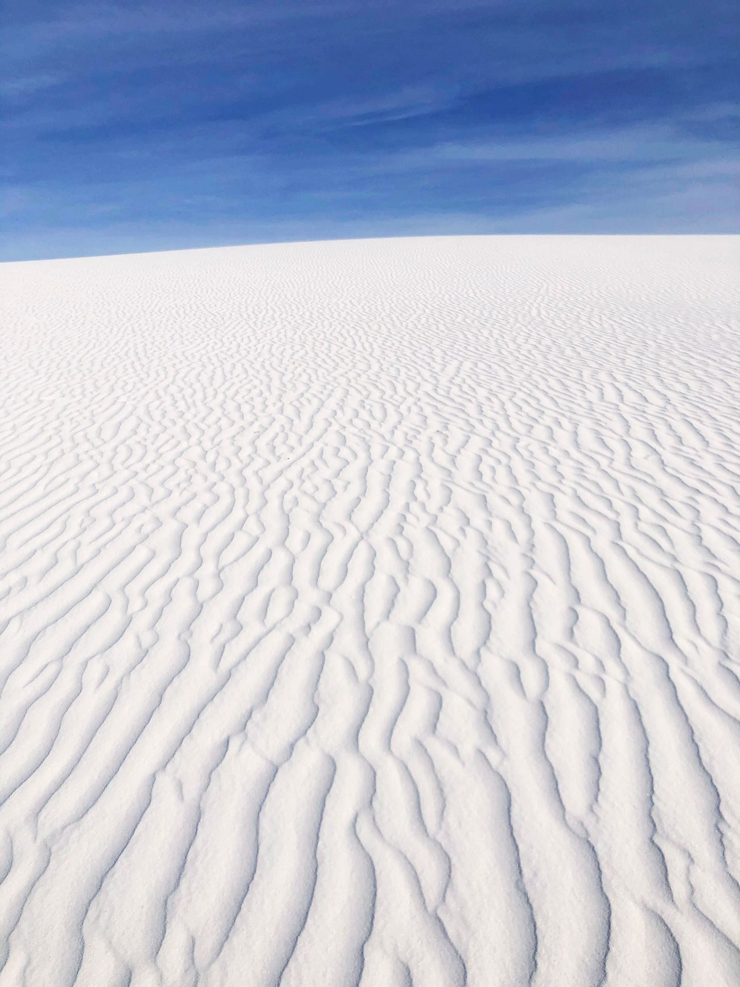 Looking up at a sand dune hill. The wind has created a curved pattern in the sand.