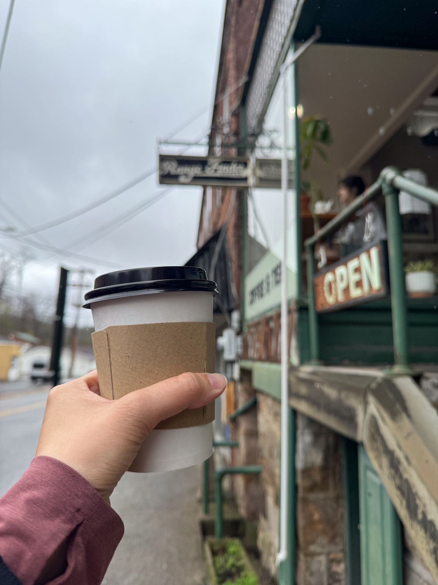 Holding up a coffee in front of the exterior of Range Finder