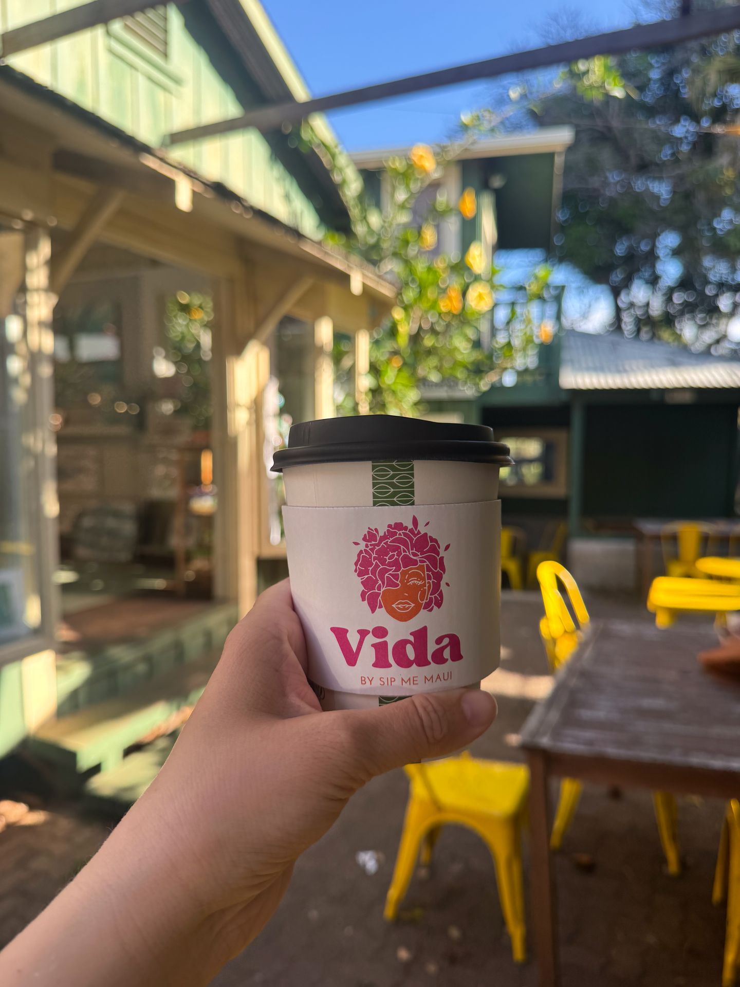 Holding up a coffee that reads Vida on an outdoor patio at Vida by Sip Me