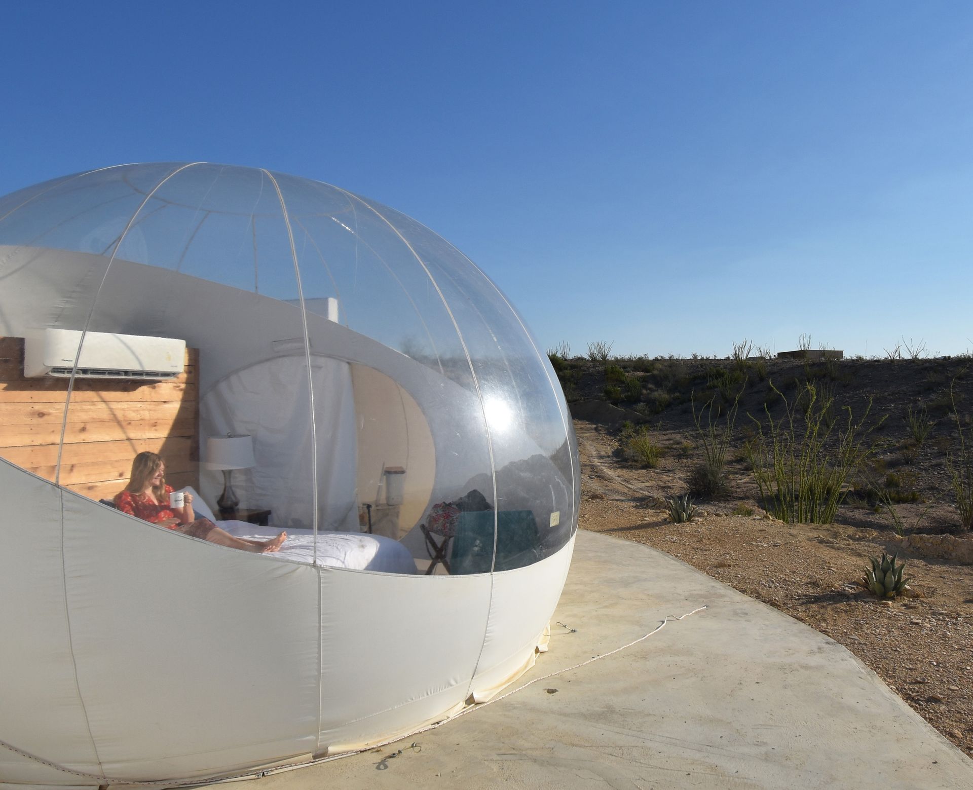 Lydia sitting inside of the bubble and drinking coffee. The photo is taken from the outside of the bubble.