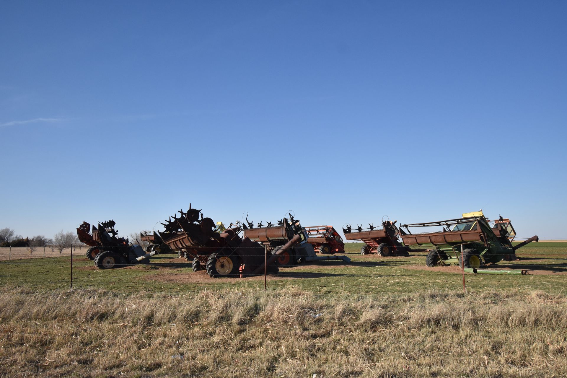 A group of combine tractors arranged next to each other behind a fence.