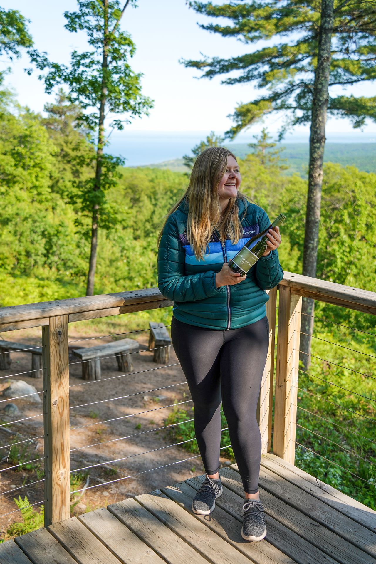 Lydia holding a bottle of wine and wearing a green Cotopaxi jacket