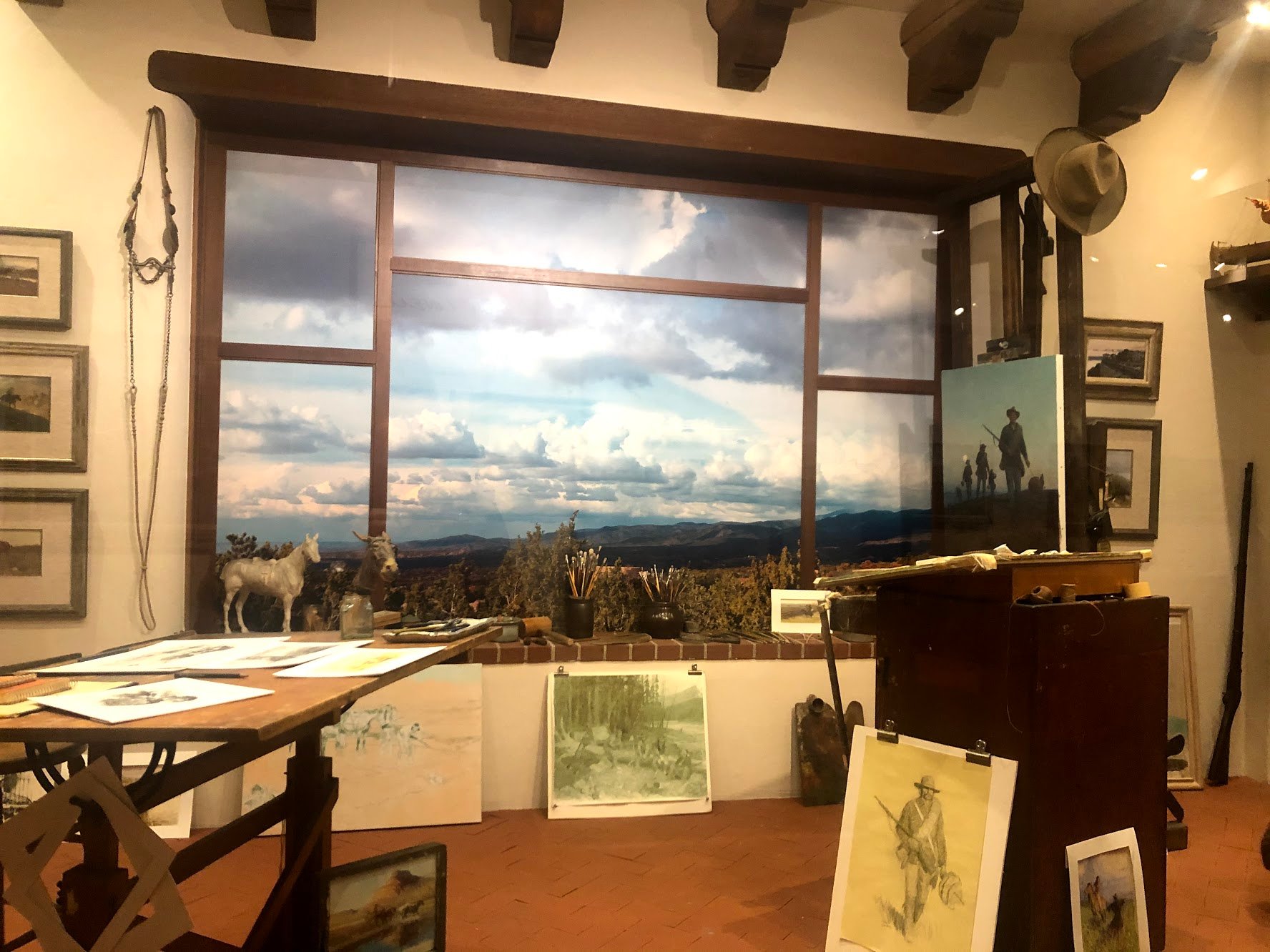 A painted wall that looks like a window with several canvas' of various paintings surrounding it. It looks like an artist studio.