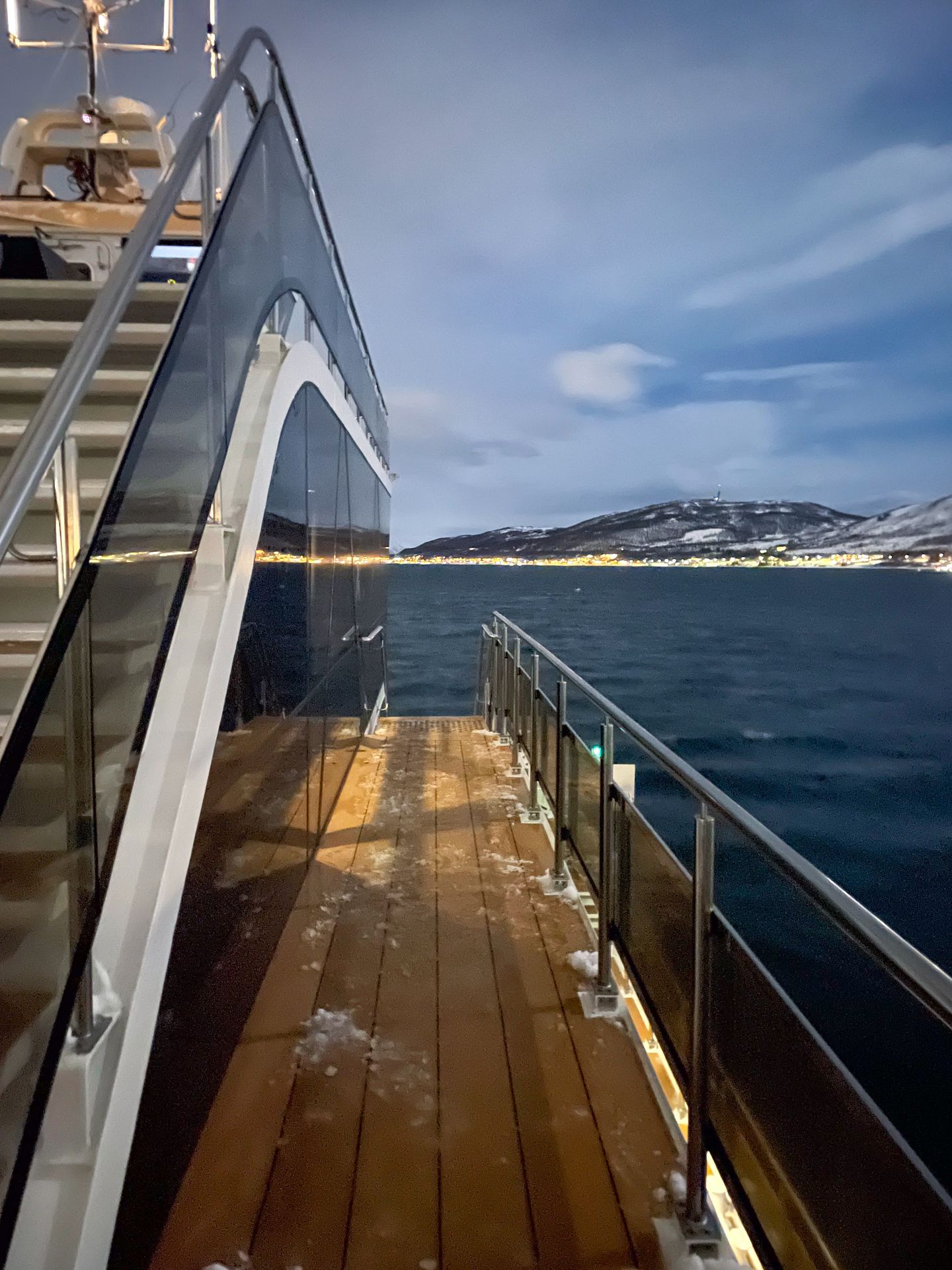 The deck from the Northern Lights cruise with Brim Explorer. There are city lights and a mountain on teh shore in teh distance