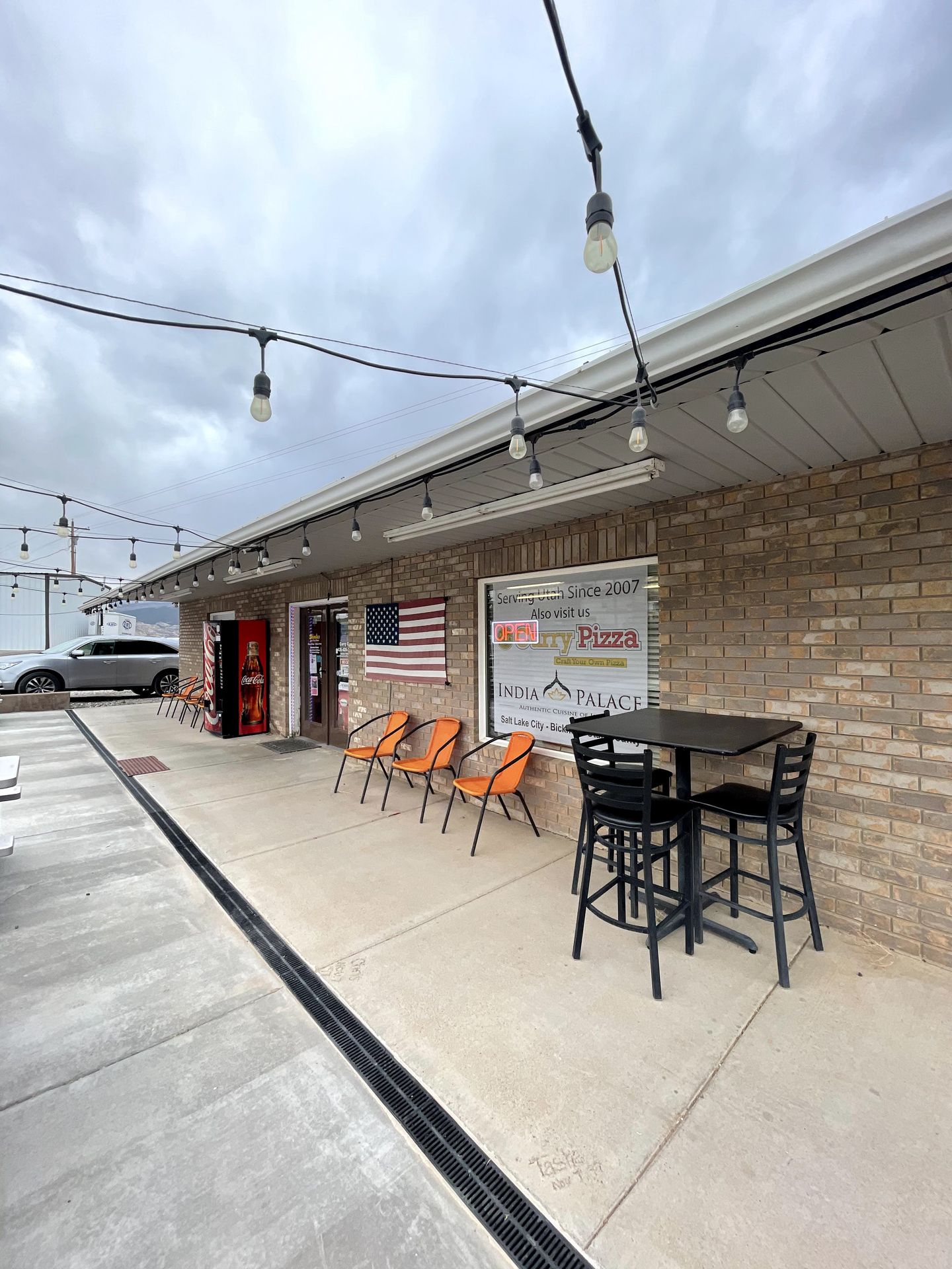 The exterior of Curry Pizza. There are some chairs outside and an American flag.