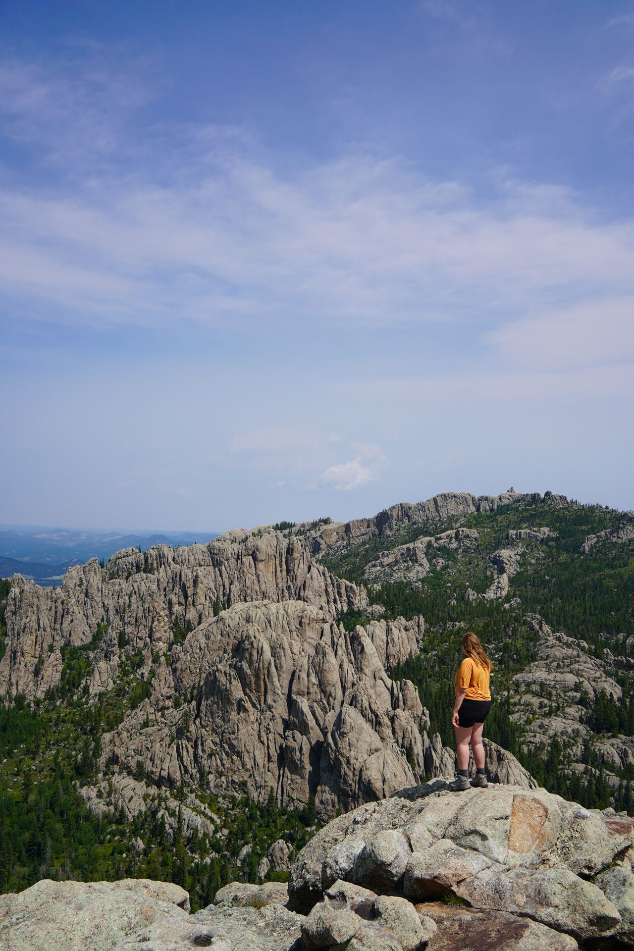 Lydia standing and looking out at a view of rocks and trees from Little Devil's Tower in Custer State Park