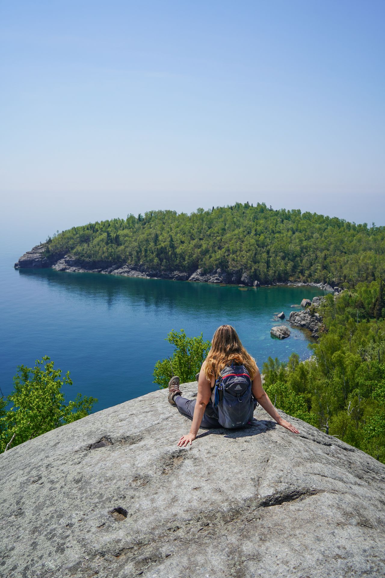 Lydia sitting on a rock and looking out at Lake Superior and a peninsula extending out into the water.