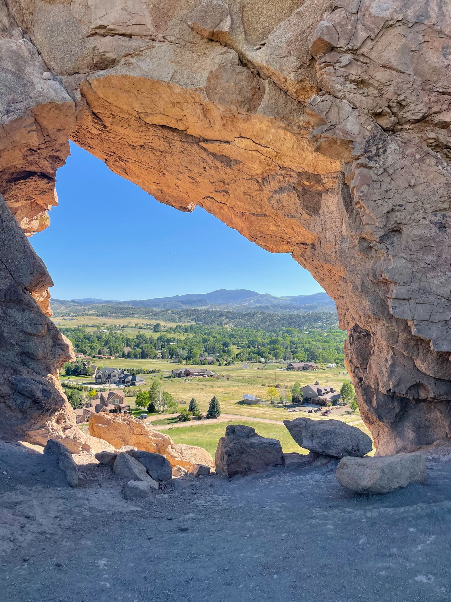 An arch made up of orange rock. The inside of the arch comes to a point in the top, left corner. There is a view of green land through the arch.