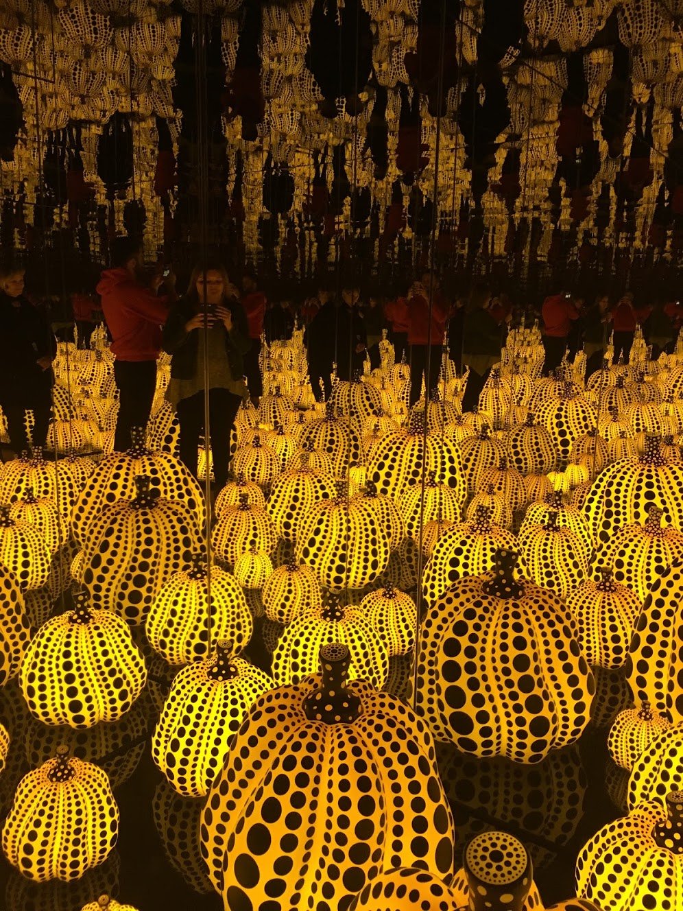 A display of neon orange pumpkins with black dots in front of a mirror from a special exhibit at the DMA.