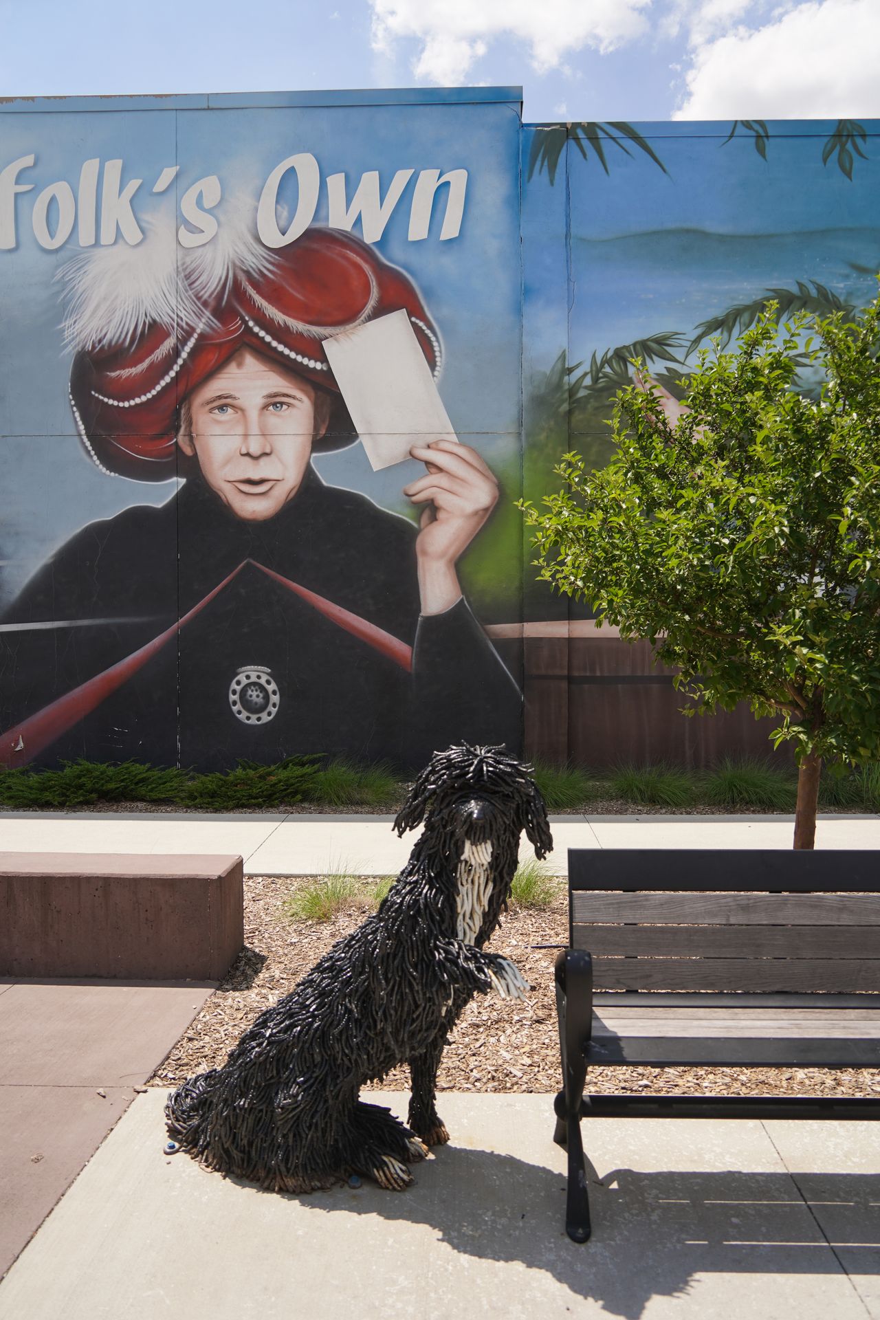 A dog statue and a bench in front of a Johnny Carson mural in downtown Norfolk
