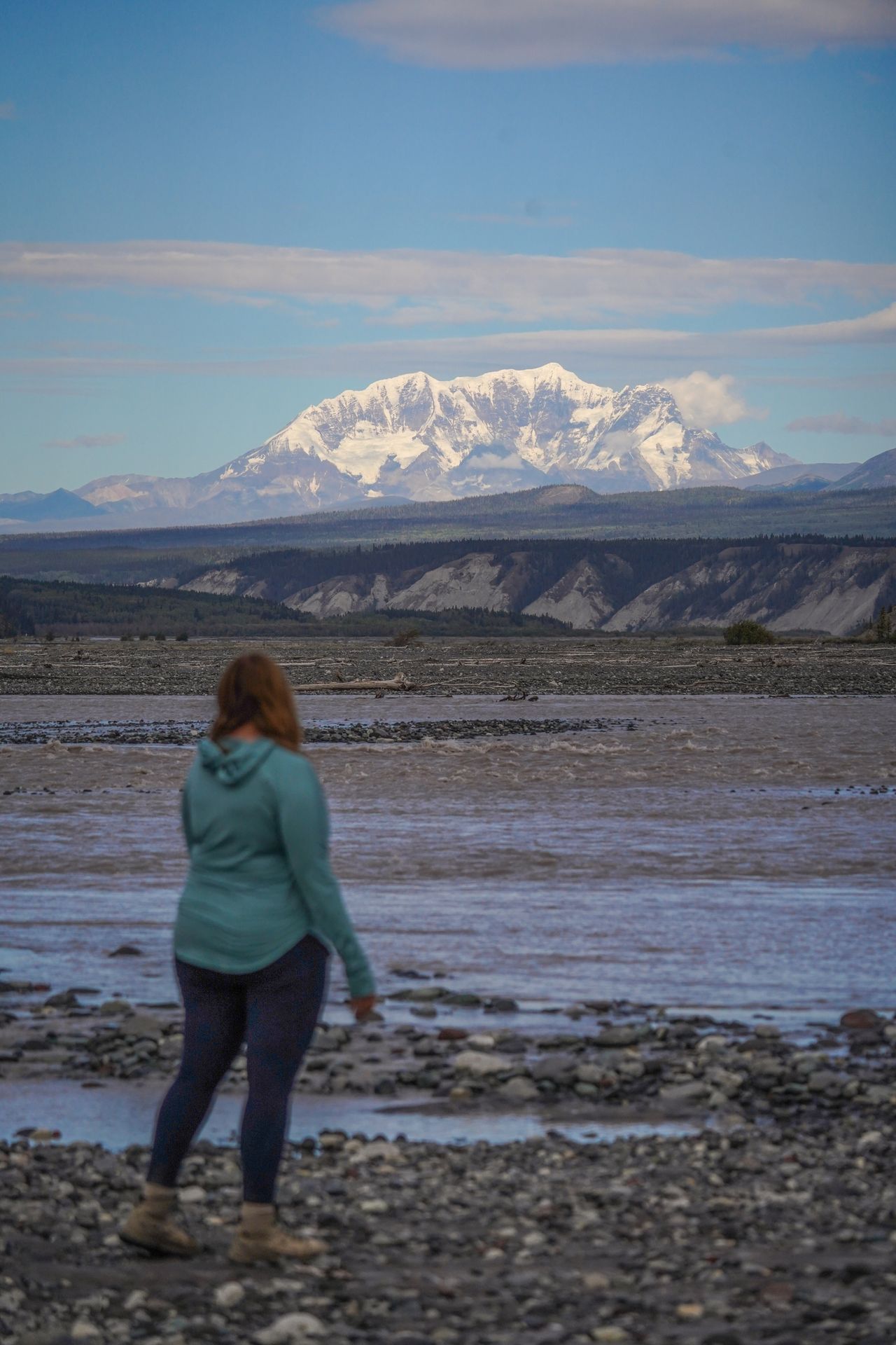 Lydia standing on the edge of a braided river and looking out at Mount Drum along the McCarthy Road