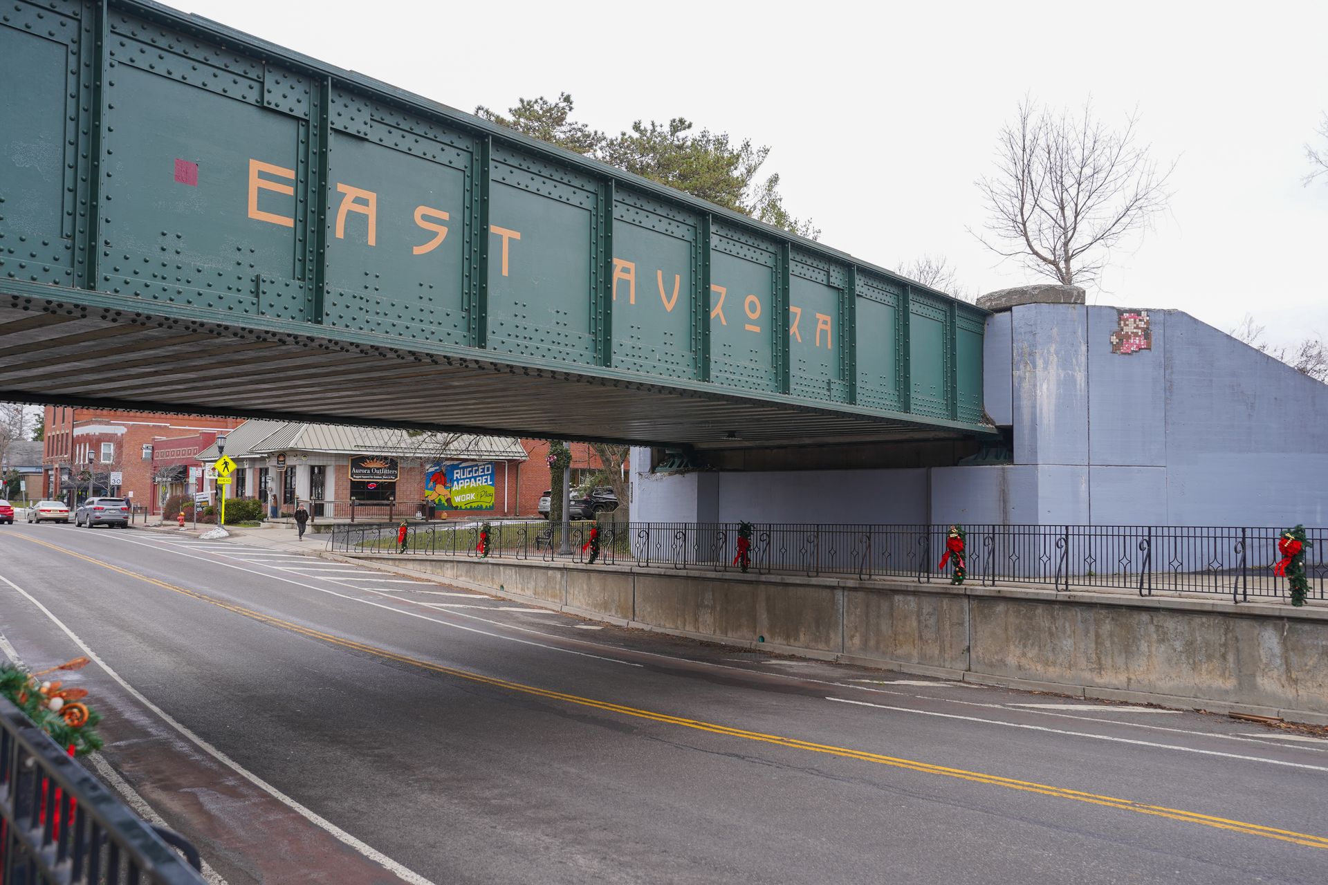A green bridge that reads 'East Aurora' in yellow letters. The bridge goes over a large road.
