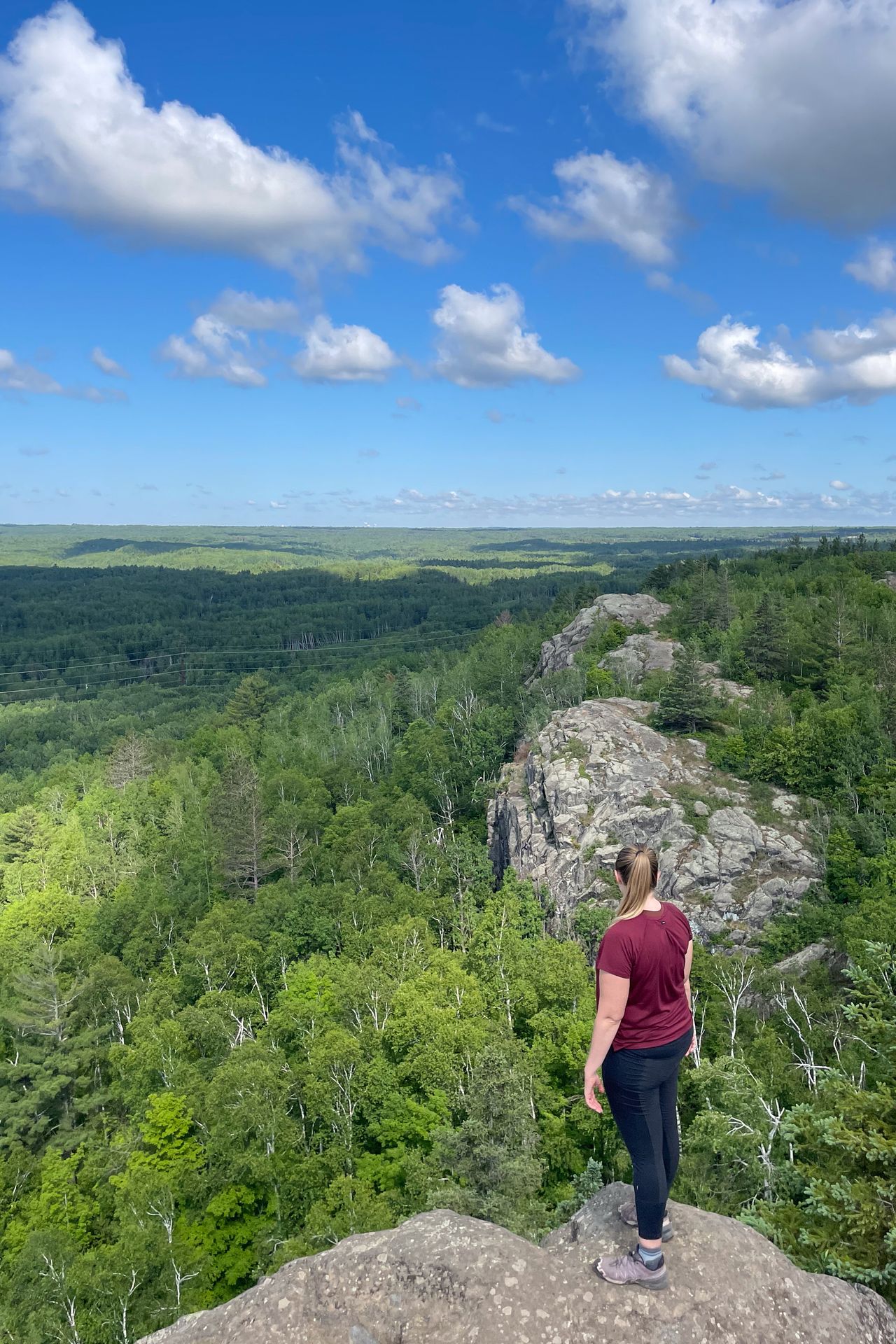 Lydia looking out at a view of green trees and some rocks from the top of Ely's Peak.