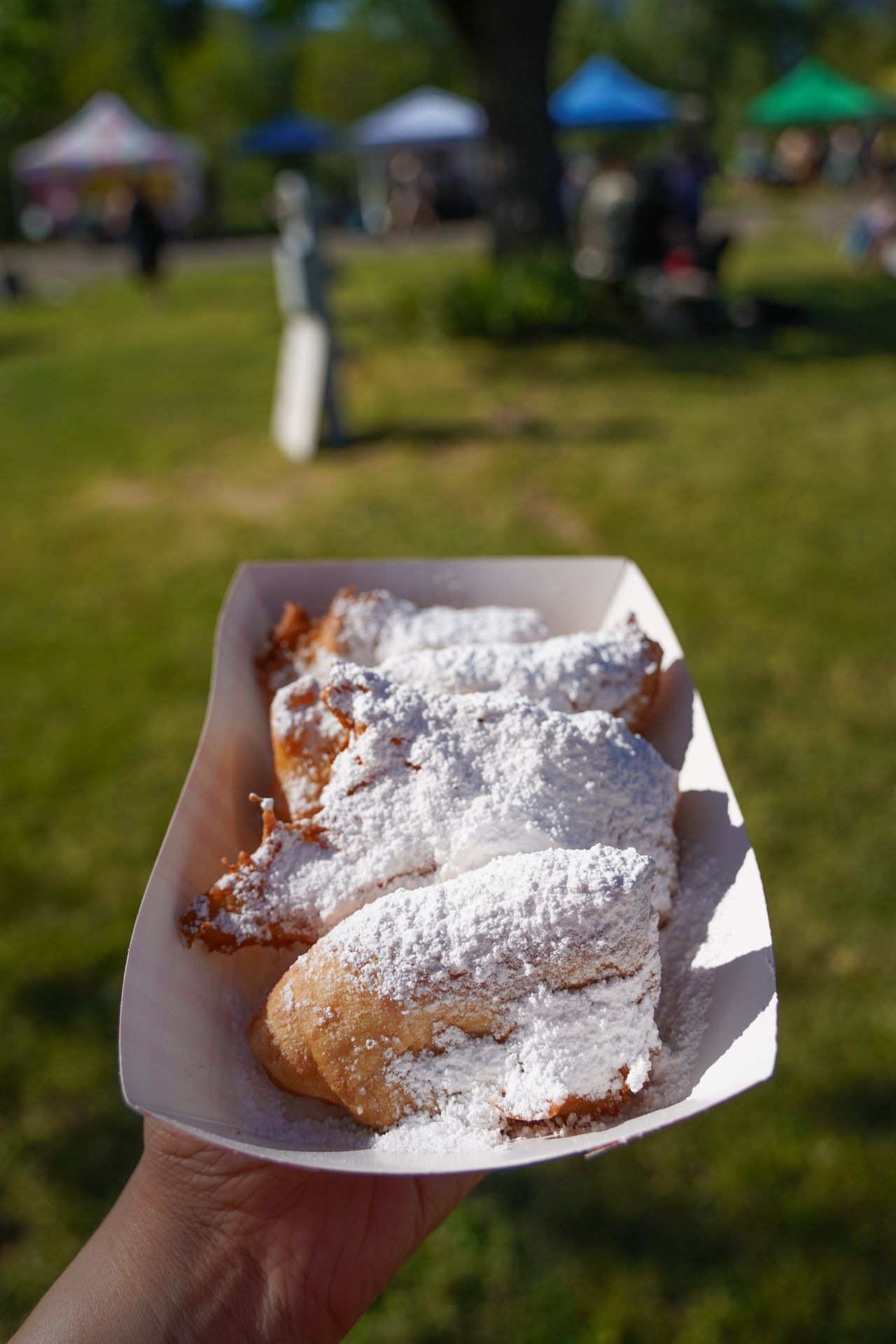 Holding up a paper bowl of beighnets at the Cave Junction Farmers Market