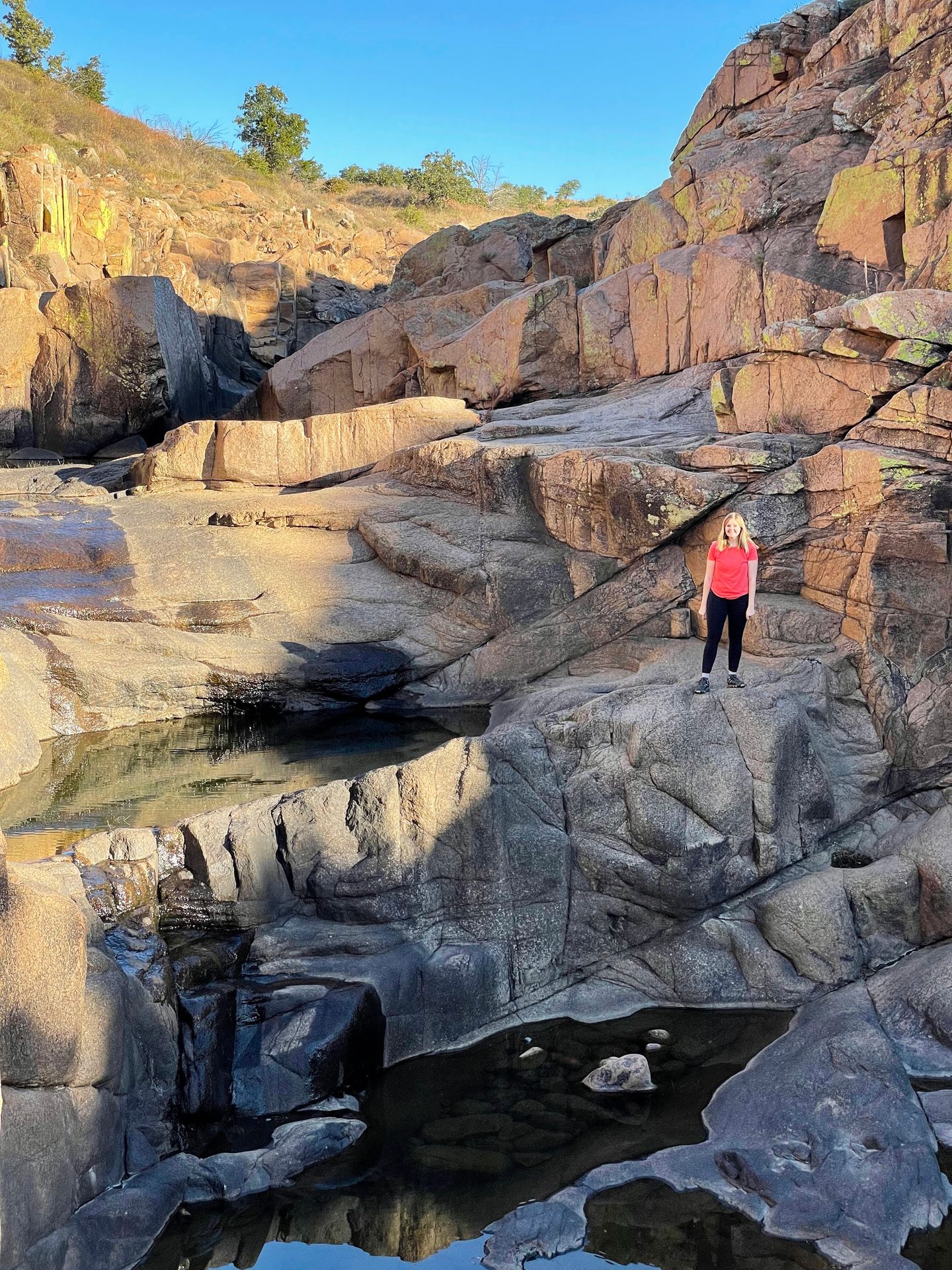 Lydia standing on rocks in the Forty Foot Hole trail. There are some pools of water in the rocks.