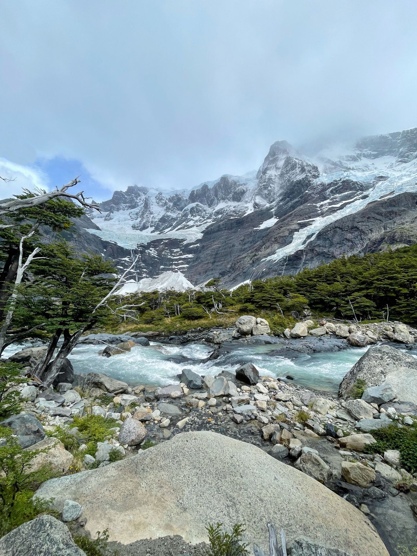 A river with light blue water flowing. There are mountains across the water with glaciers.