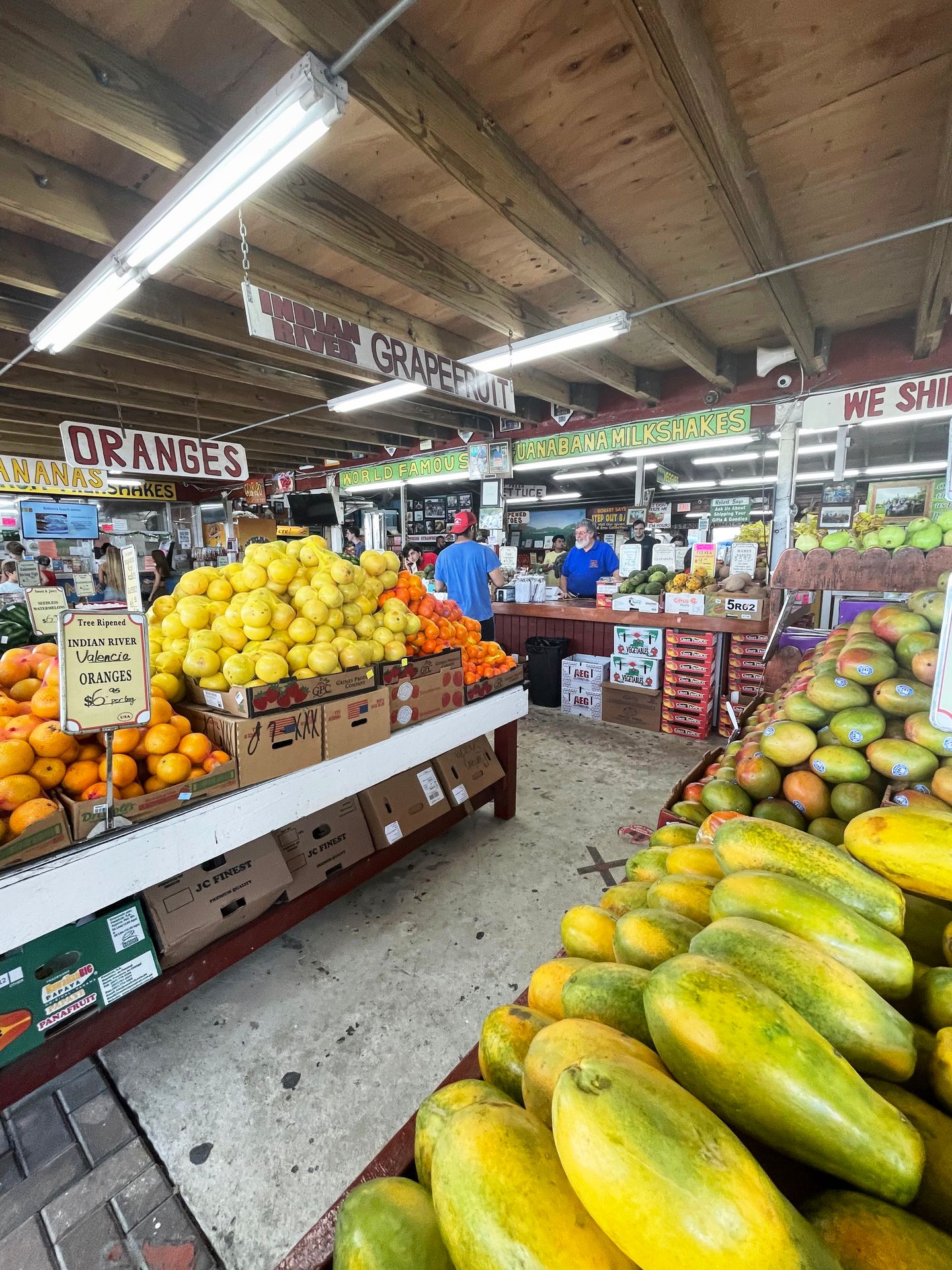 Colorful fruit laid out for sale at Robert is Here. There are oranges, mangoes and lemons. Robert wears a blue shirt and is working behind the counter.