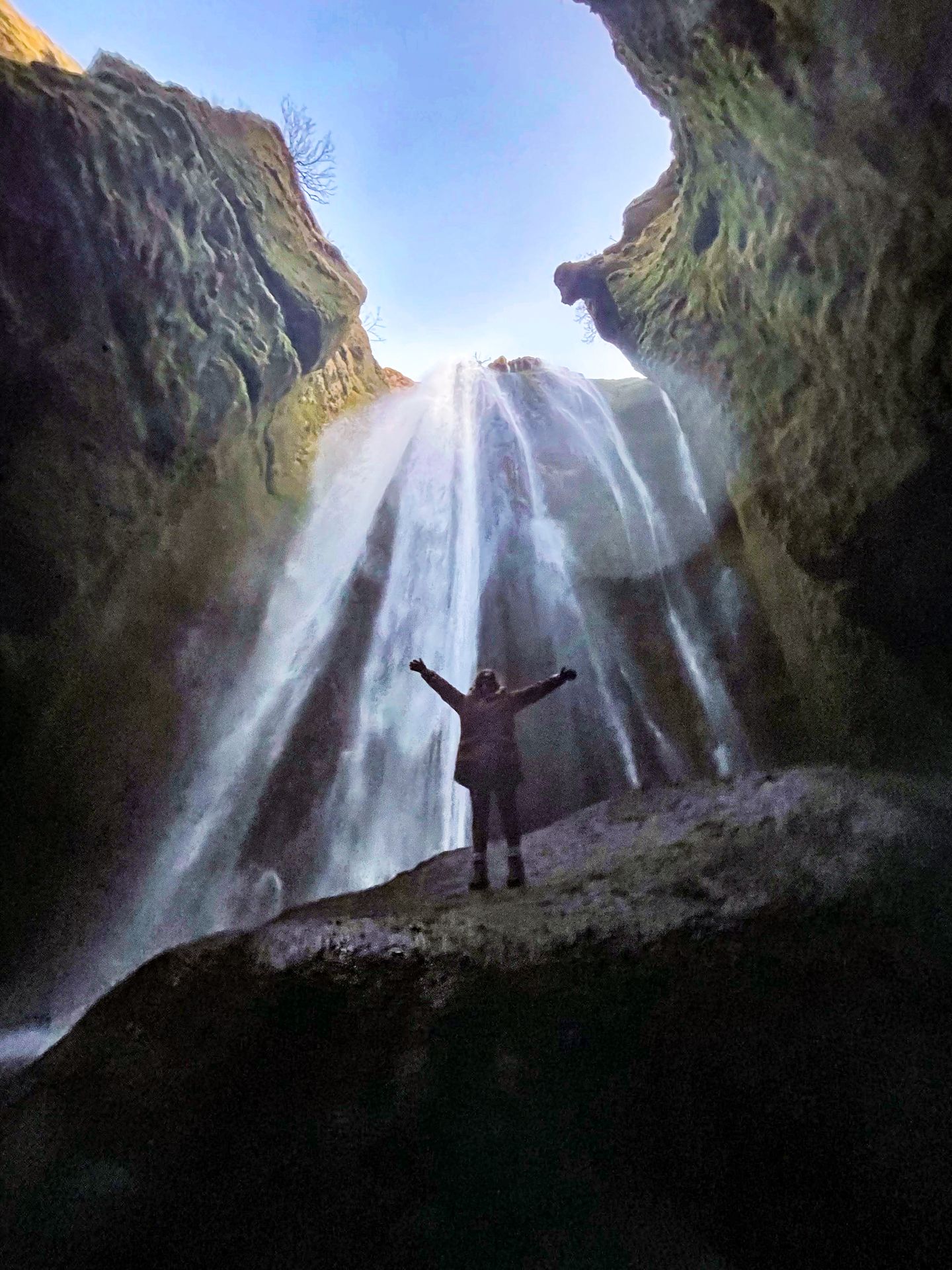 Lydia standing on top of a giant boulder in a canyon with a waterfall behind her.