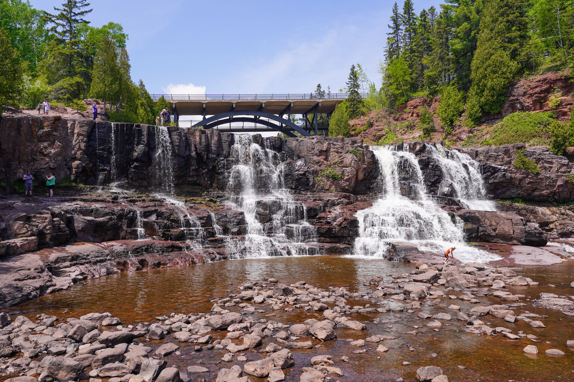 A large cliff with water flowing down in a few areas. There are people at the top and bottom of the falls.