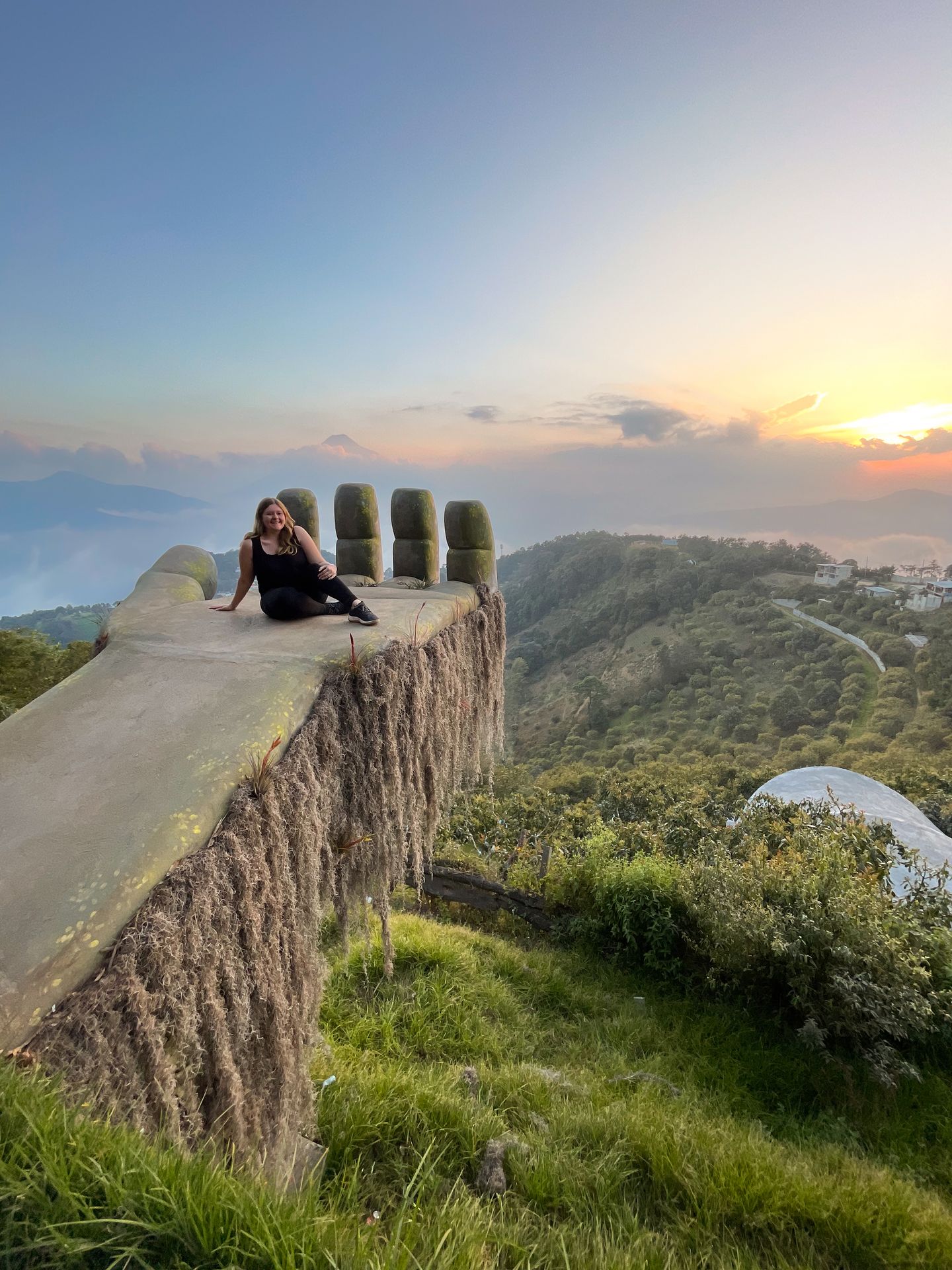 Lydia sitting on the 'Hobbit Hand' at Hobbitenango at sunset