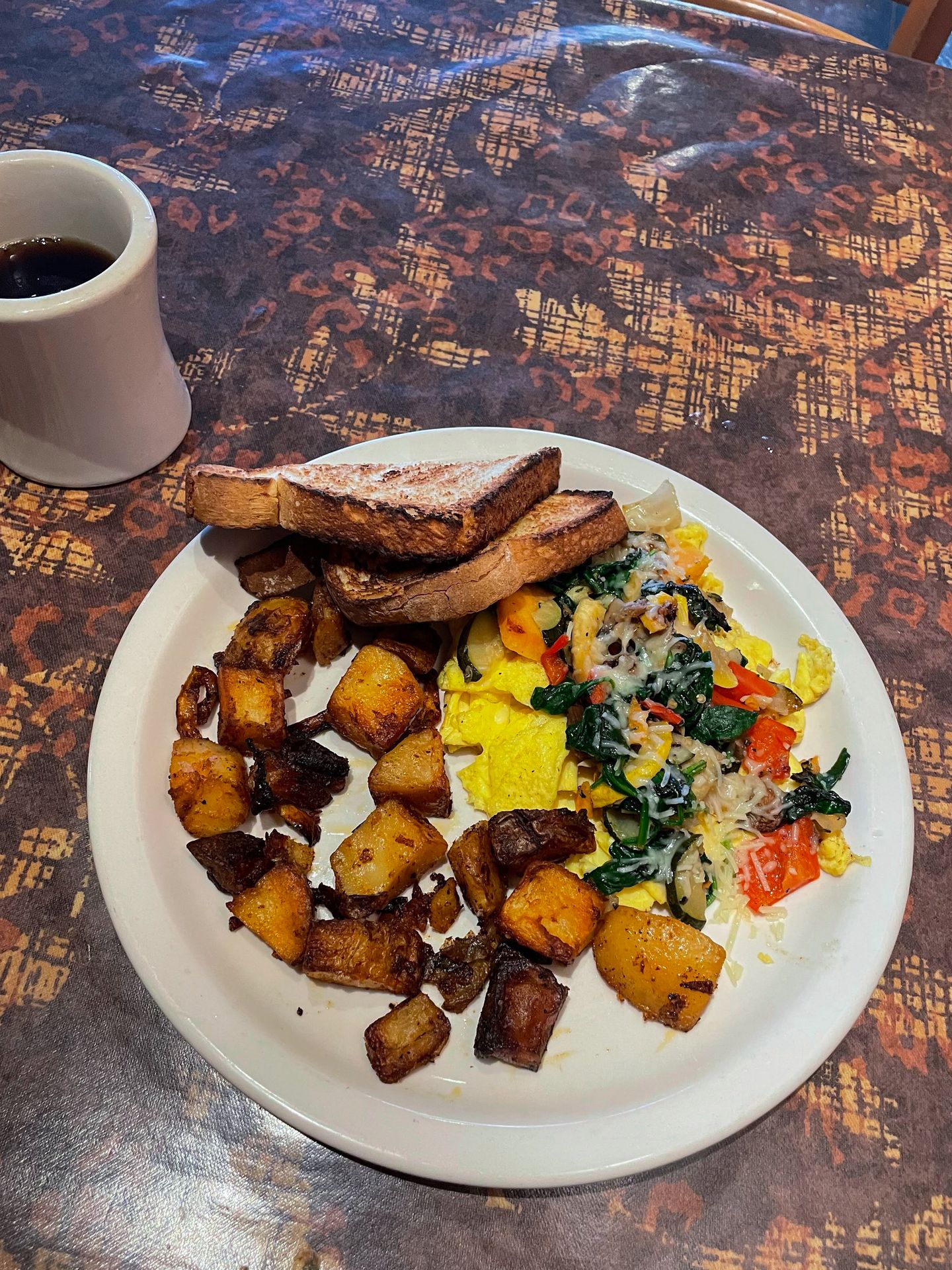 A plate of hashbrowns, scrambled eggs and toast next to a mug of coffee.