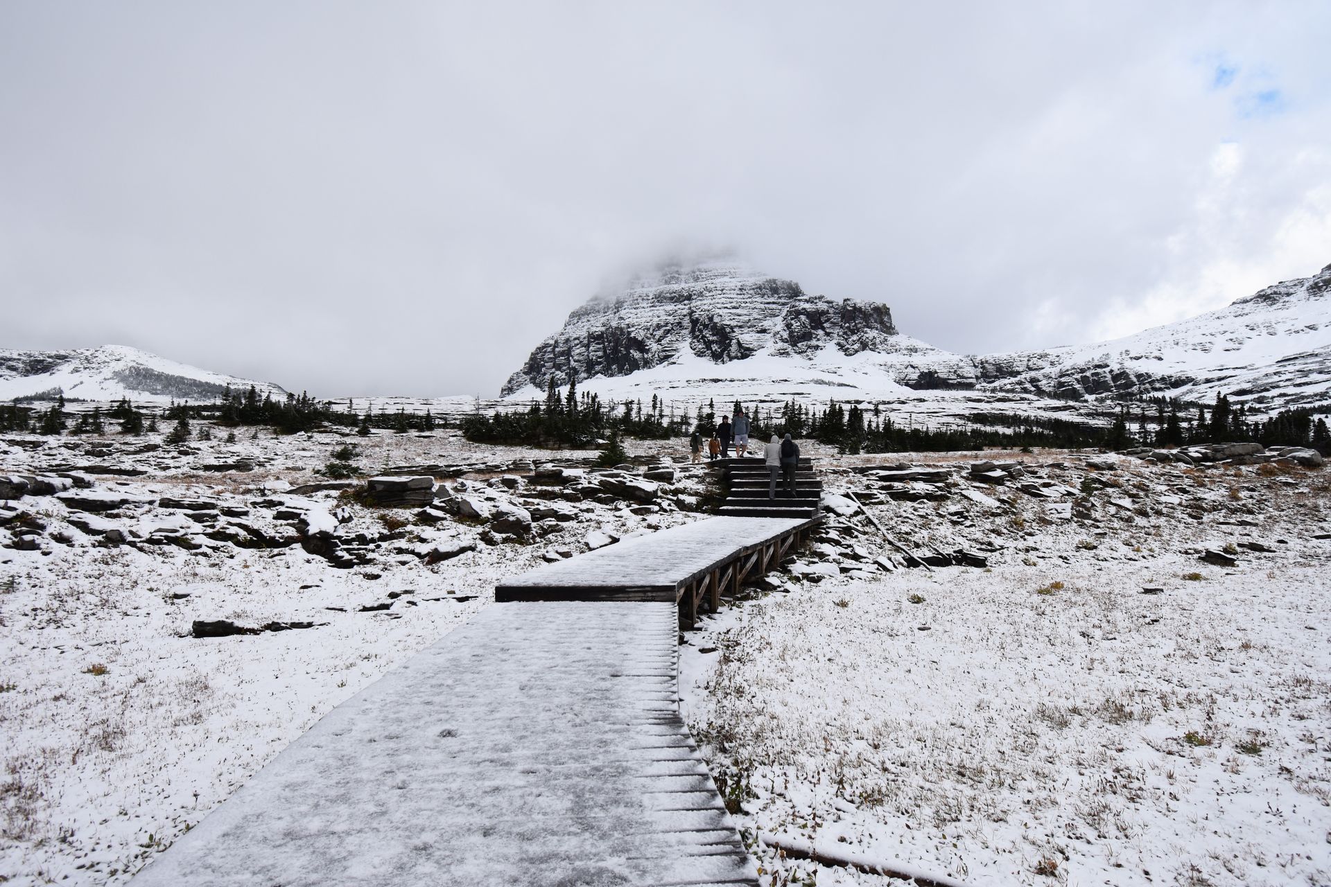 A snow covered boardwalk trail leading up to a mountain.