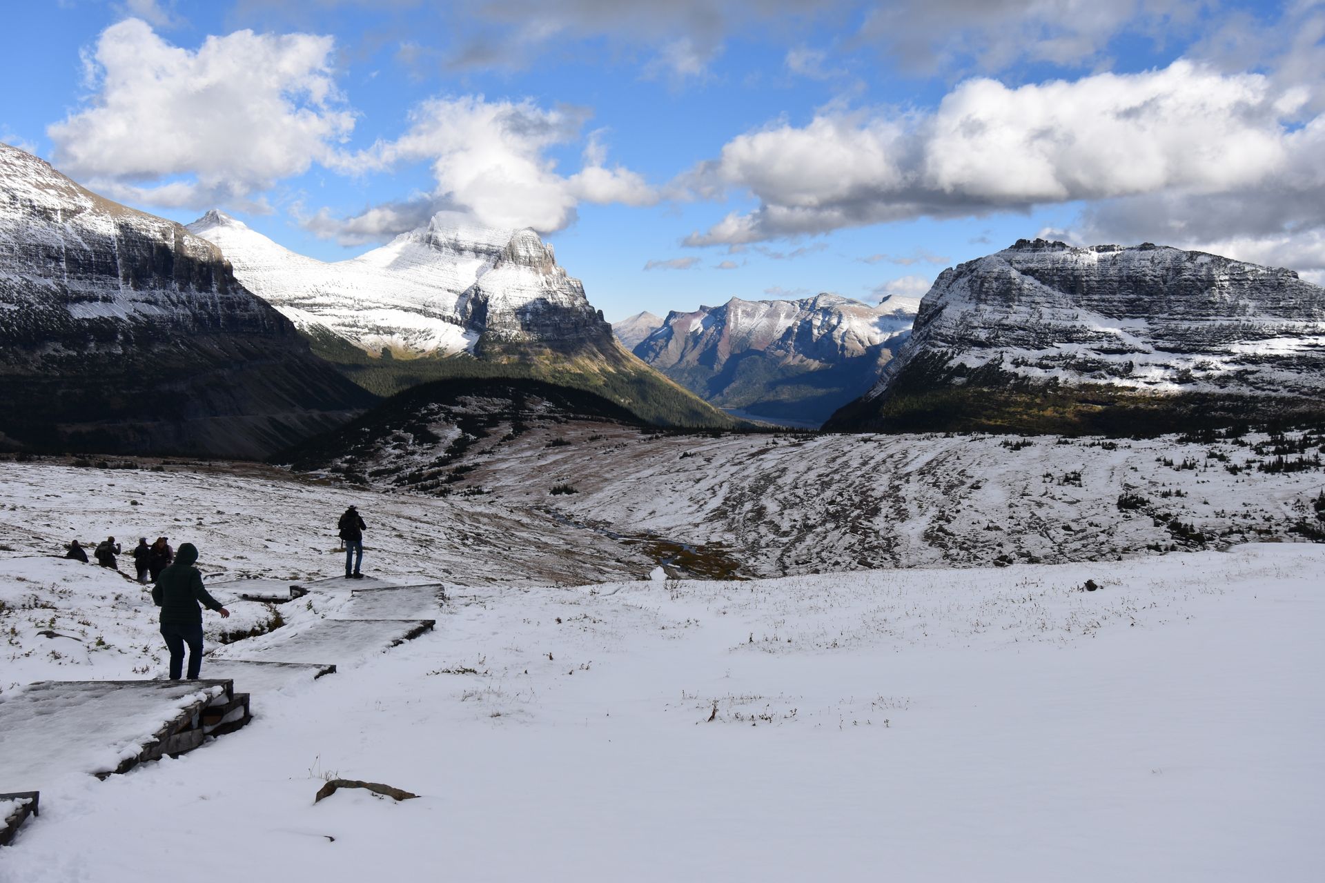 Hikers on a snowy boardwalk trail hiking down from Hidden Lake. There are mountain views in the distance.