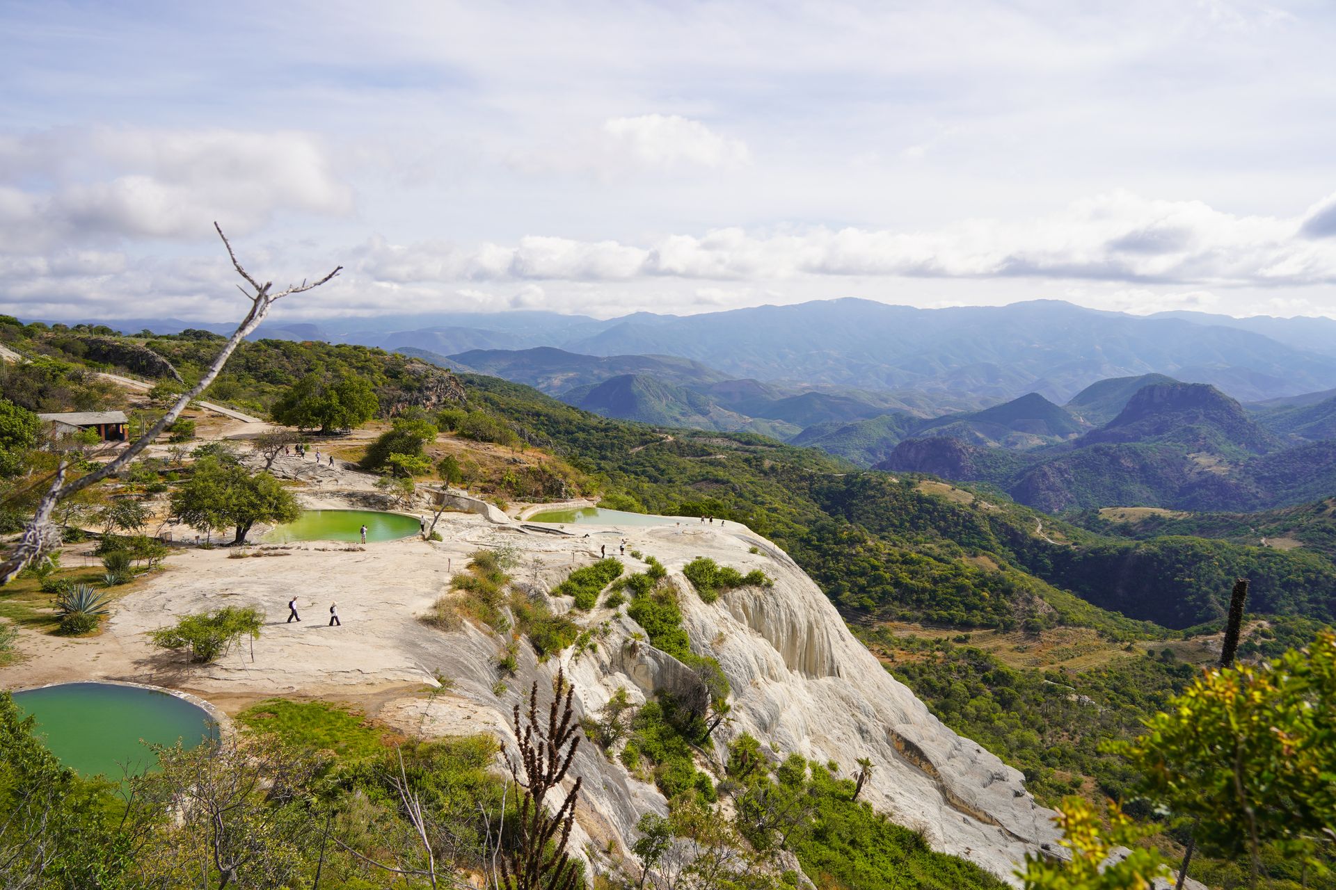 Looking down at Hierve el Agua, which has white rocks, pools of waters and mountains in the distance