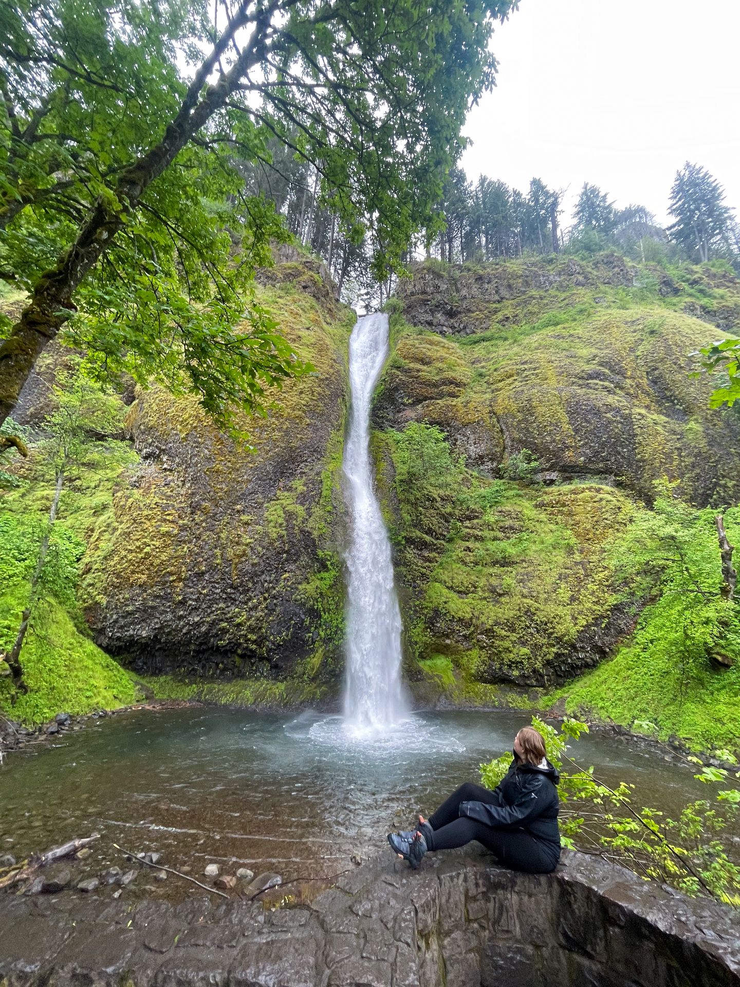 Lydia sitting on a stone wall looking at Horsetail Falls