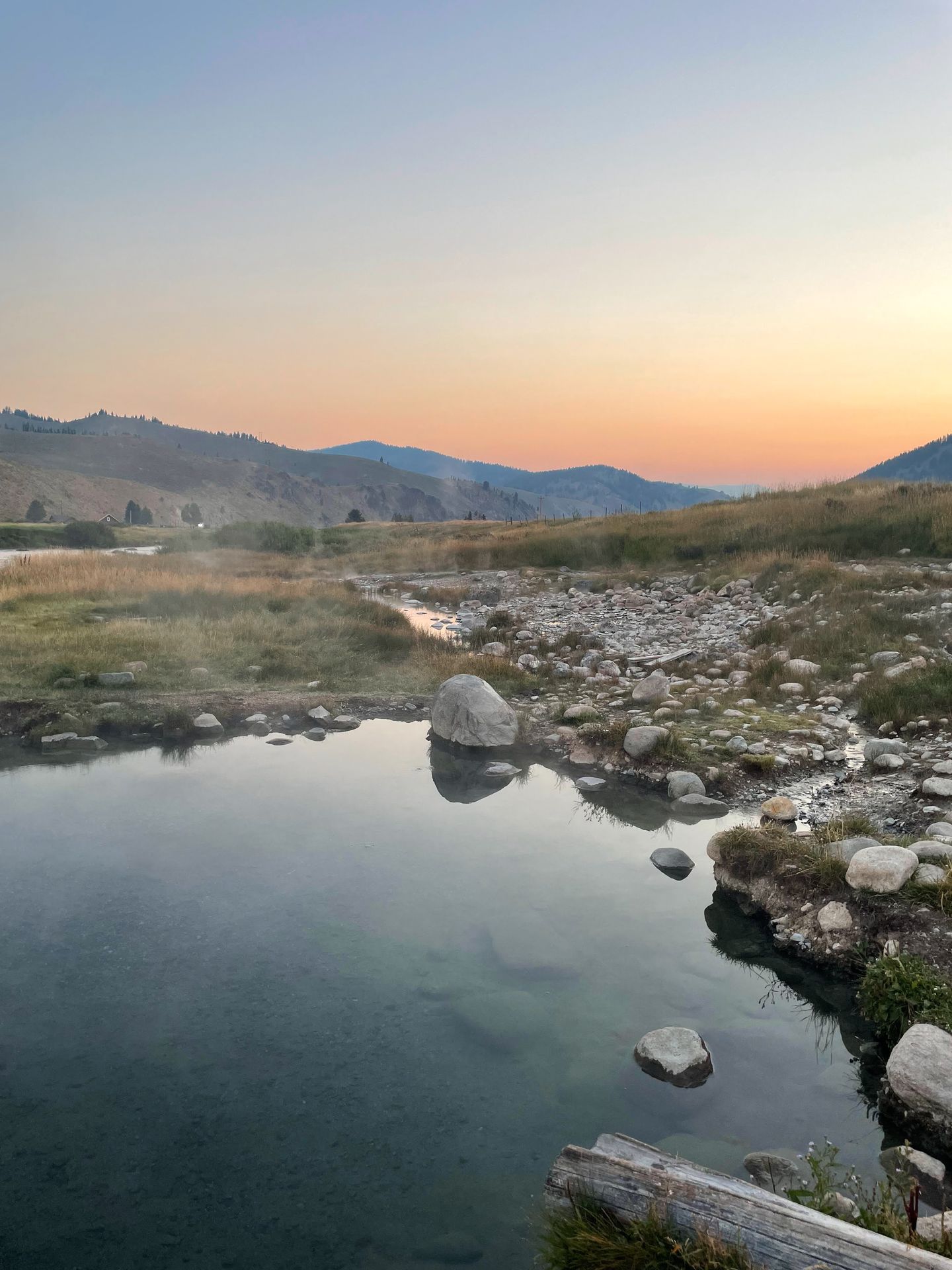 Looking out at calm hot spring with mountains in the distance at sunrise.