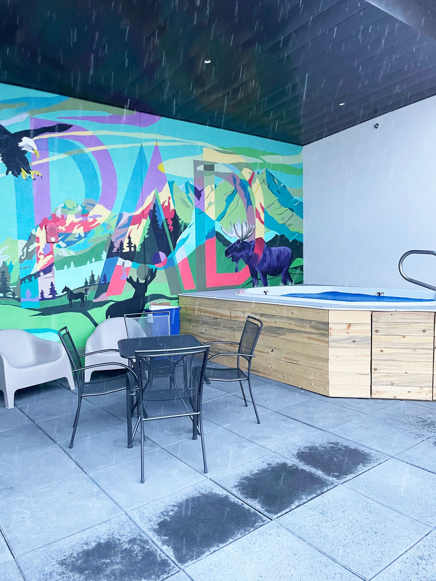 The hot tub at The Pad. There is a colorful mural behind the hot tub that says The Pad and has moose, an eagle and other wildlife in a mountain scene.