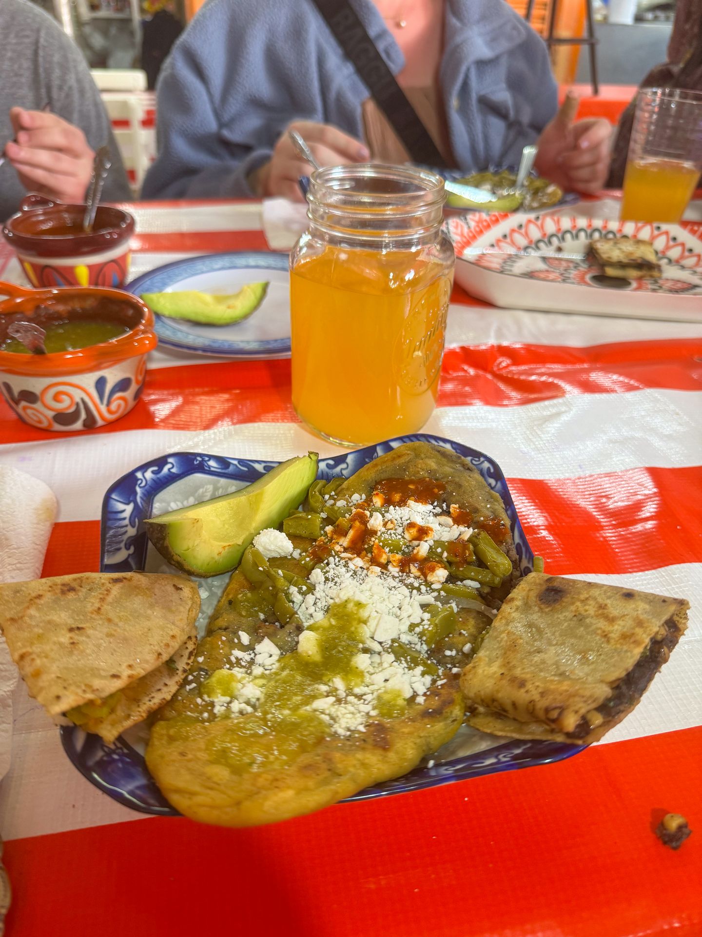 A huarache sitting on a table with a striped table cloth. It sits on a plate next to quesadillas.