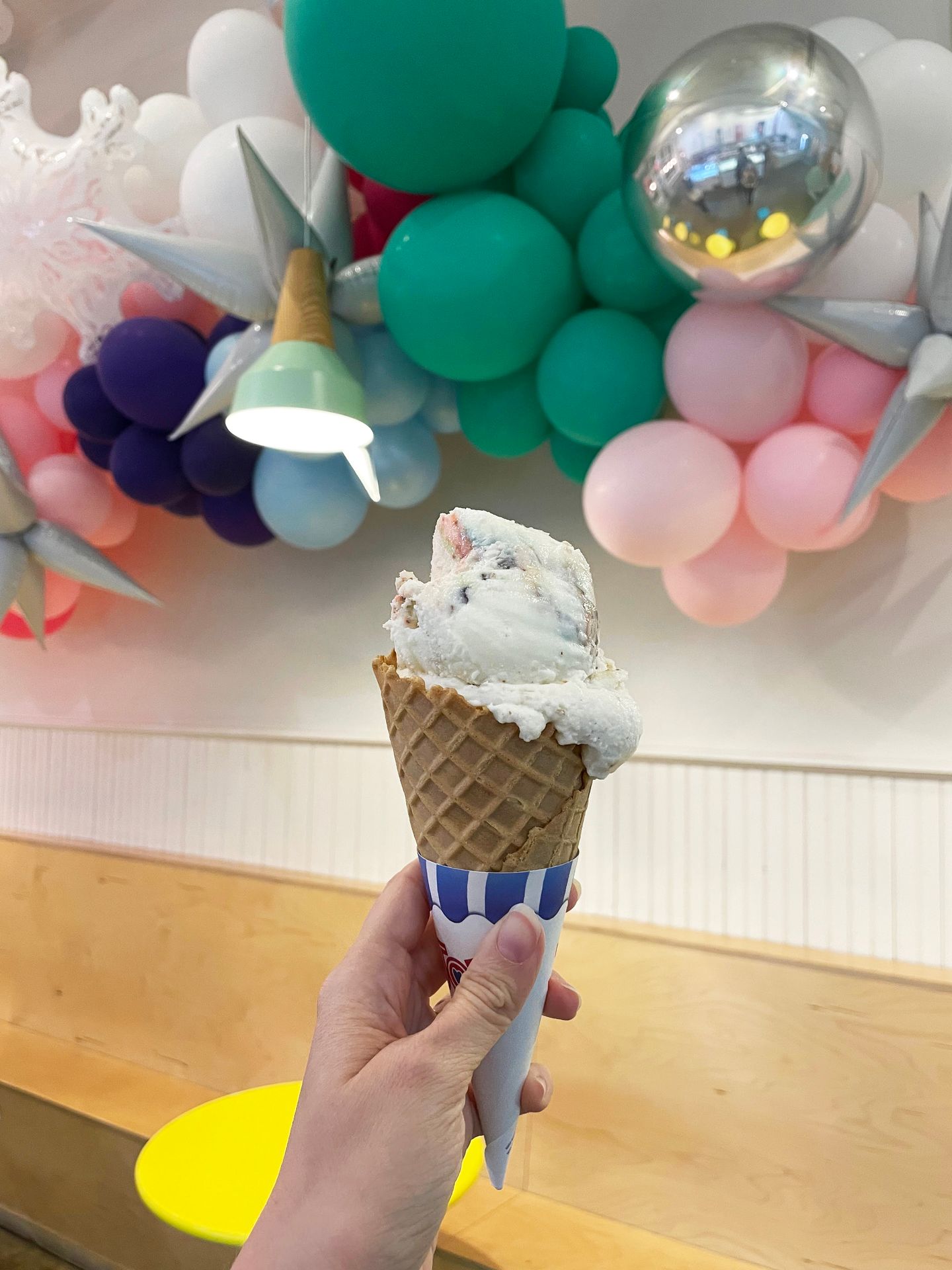 Holding up an ice cream cone in front of some colorful balloons in Loblolly.