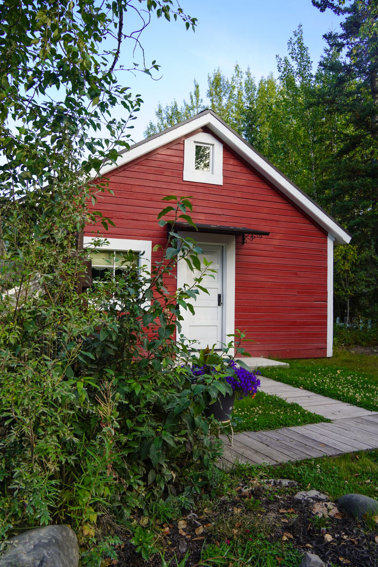 A small red house with a white door, with some greenery in front of the home