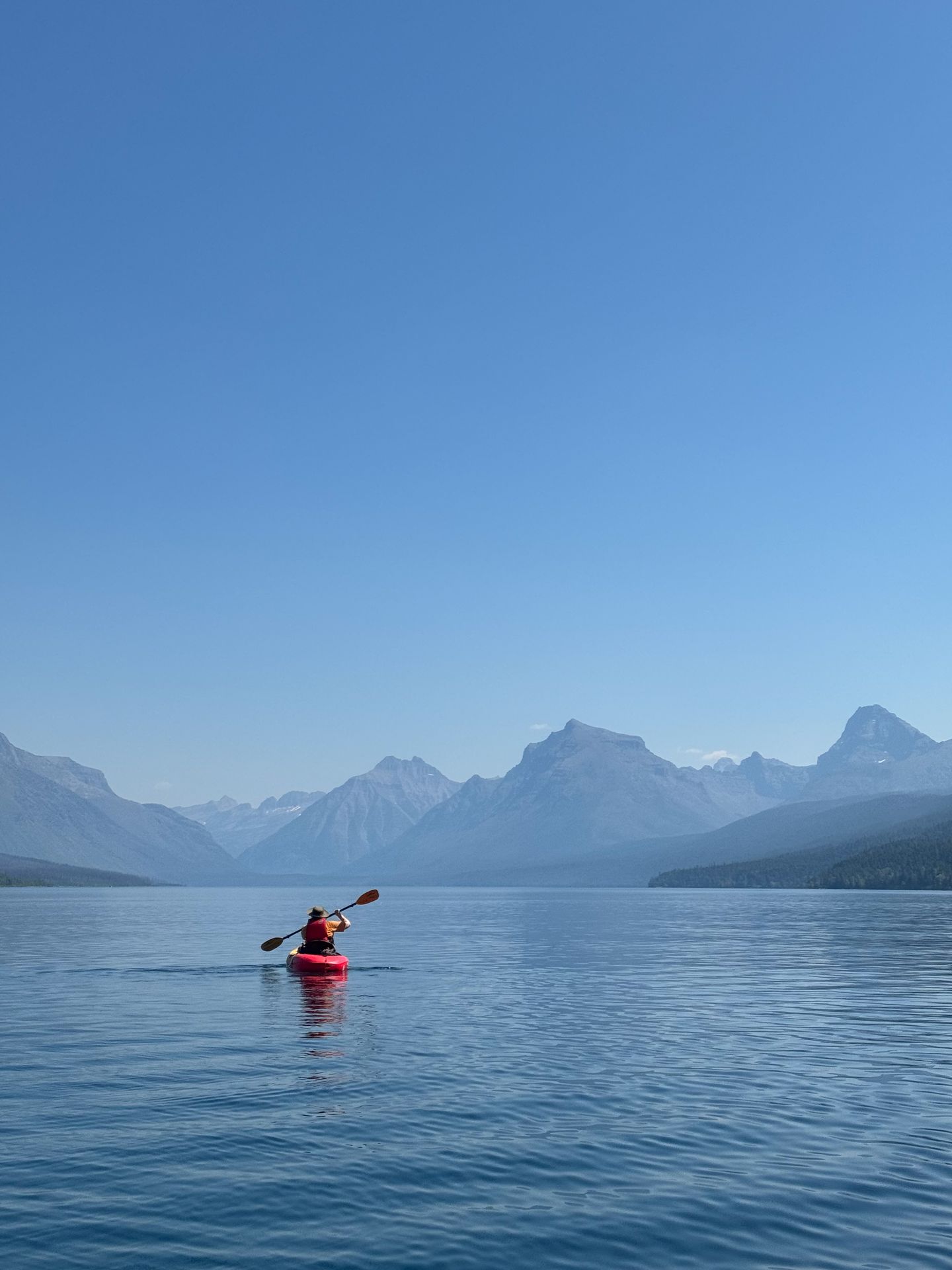 Lydia kayaking away on Lake McDonald. There are mountains in the distance.