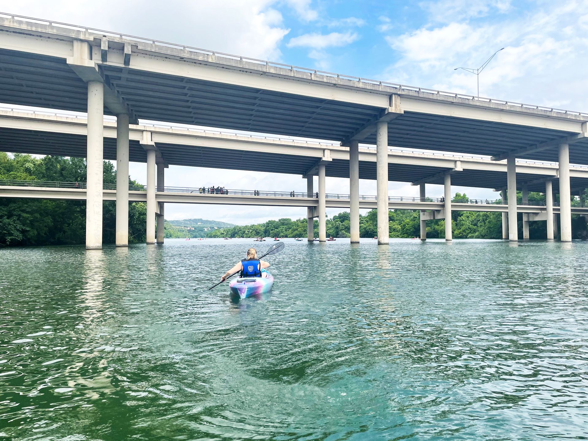 Lydia kayaking under a large bridge in Lady Bird Lake.