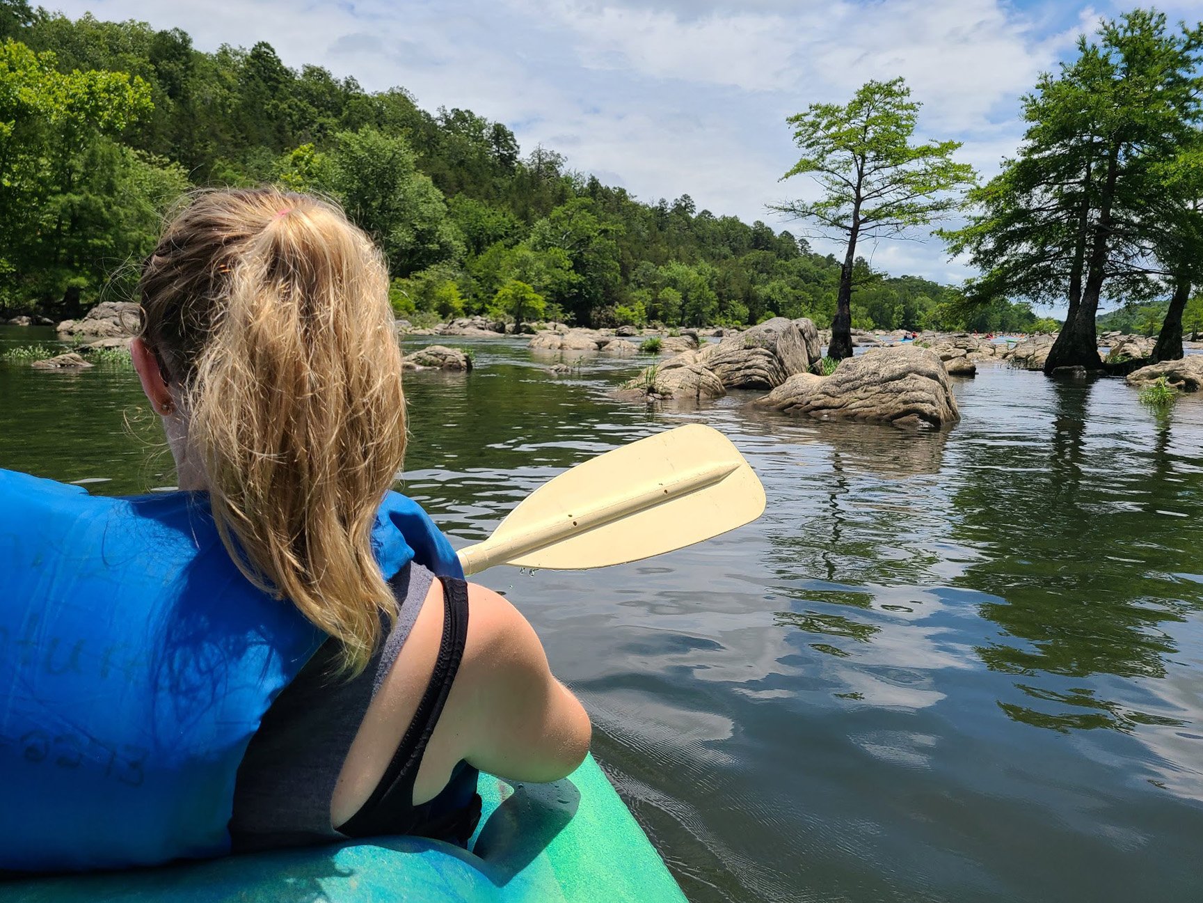 Looking at Lydia from behind while kayaking. There are some large rocks in the water nearby.