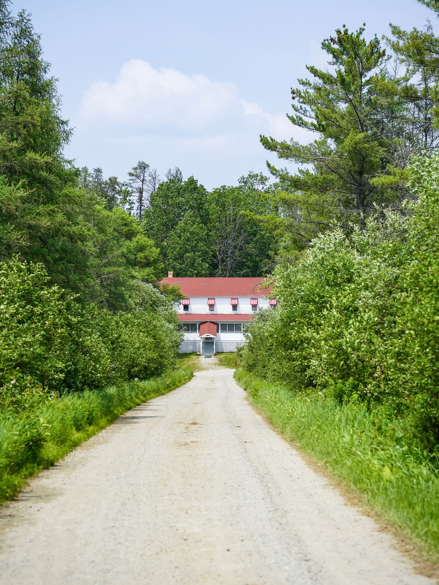 A driveway leading to the Kettle Falls hotel, which is a white building with a red roof and awnings