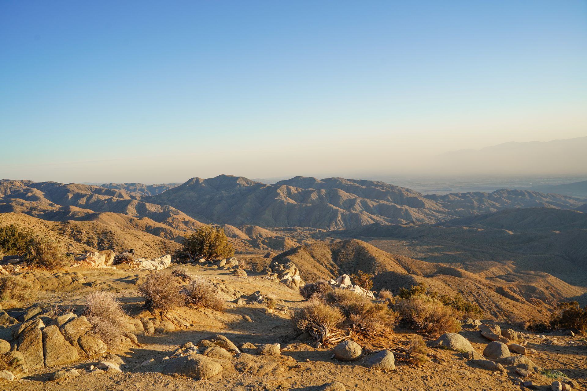 A view of mountains glowing orange at sunset from Keys View. The mountains in the far distance are obscured by haze.