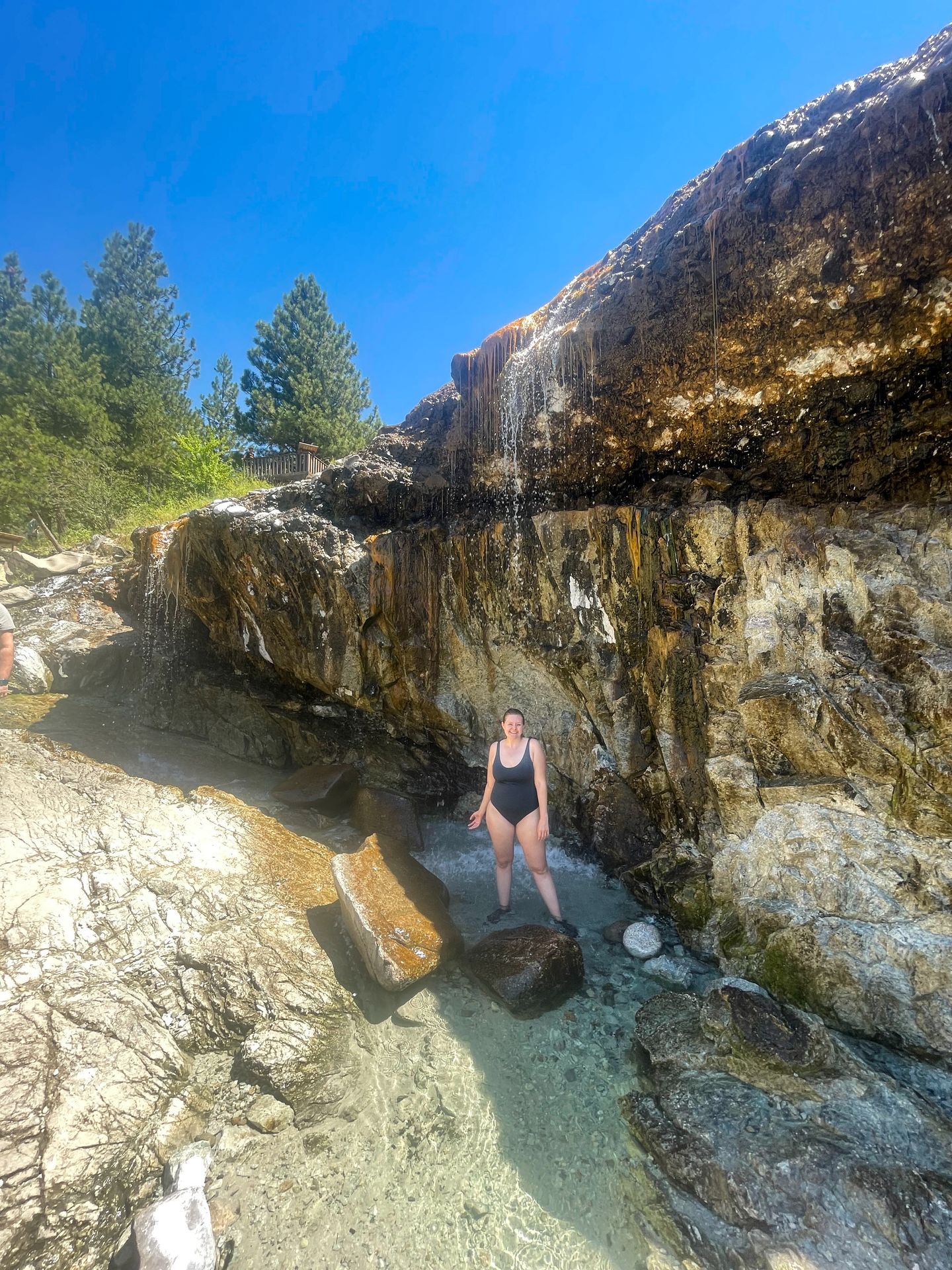 Lydia standing in a pool of water in front of a rock wall. There is a waterfall coming from over the ledge.