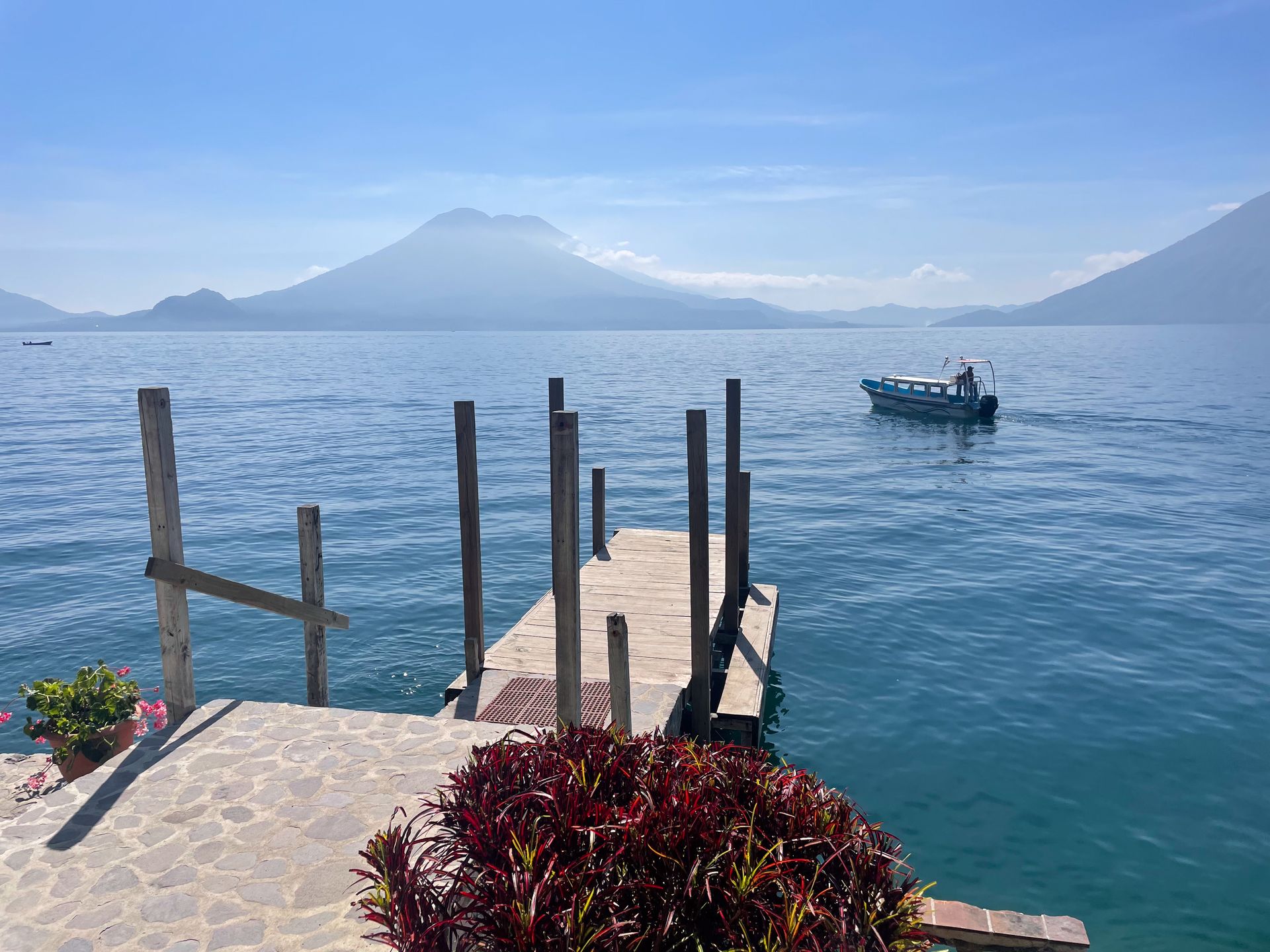 A dock on Lake Atitlan, with a boat in the distance. You can see mountains on the opposite side of the lake