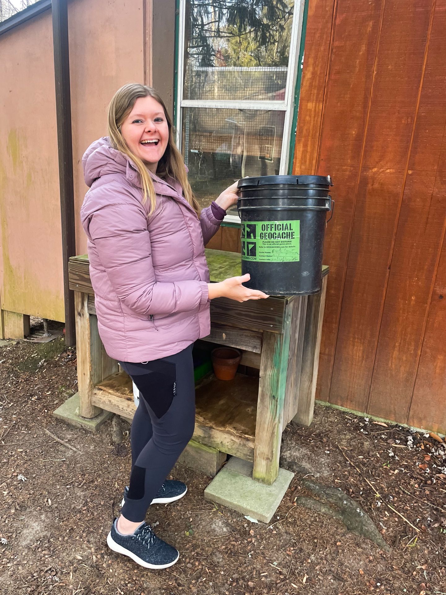 Lydia holding a large bucket labeled as an 'official geocache'