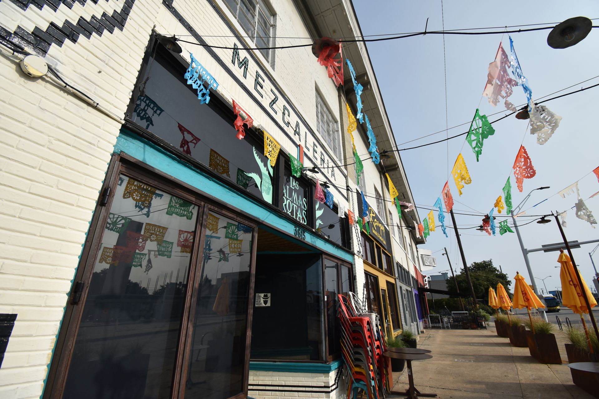 The exterior of Las Almas Rotas. The building is white and there are colorful flags hanging from it.