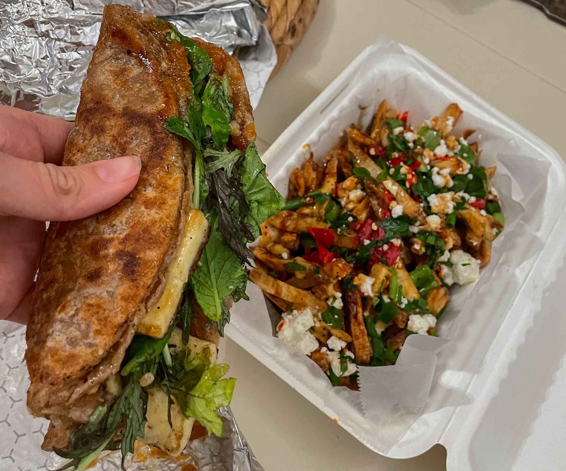 Holding up a "Malawach" from Lev Kitchen with a container or fries on the table below.