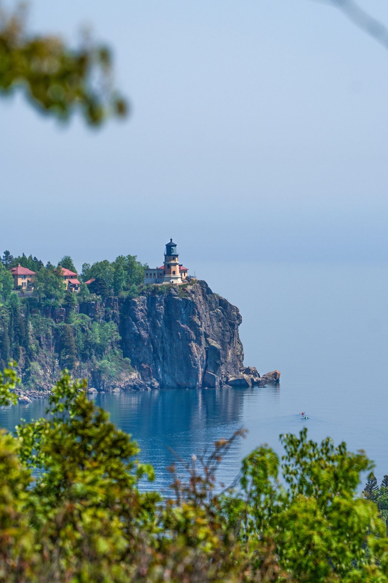 Split Rock Lighthouse in the distance, framed with a few tree leaves from the top of Day Hill.