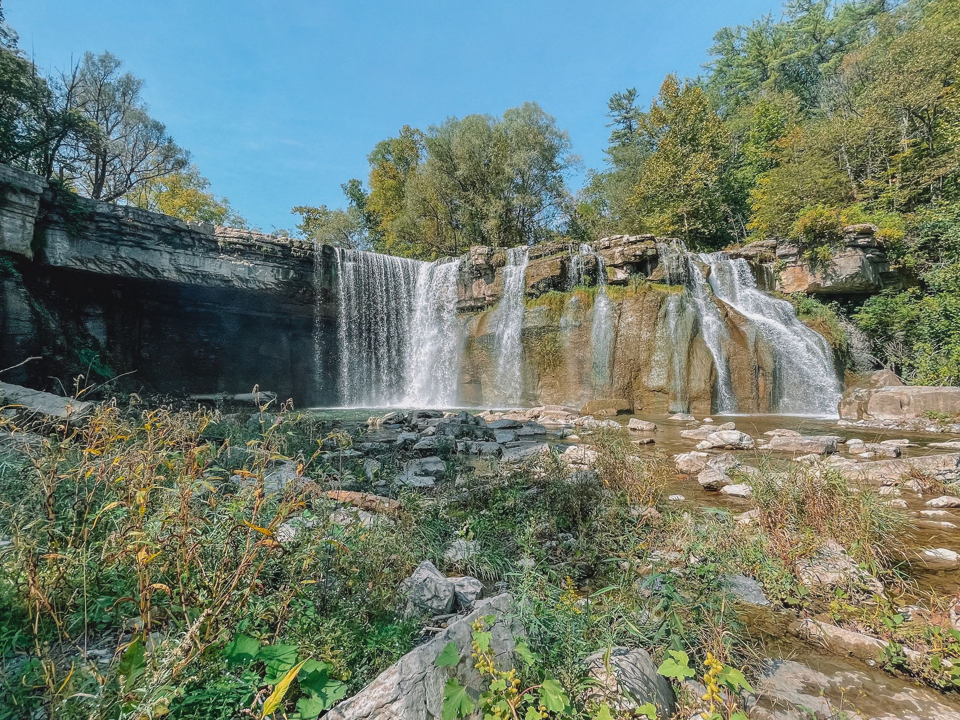 Looking down at a wide waterfall with a cliff overhang on one side.