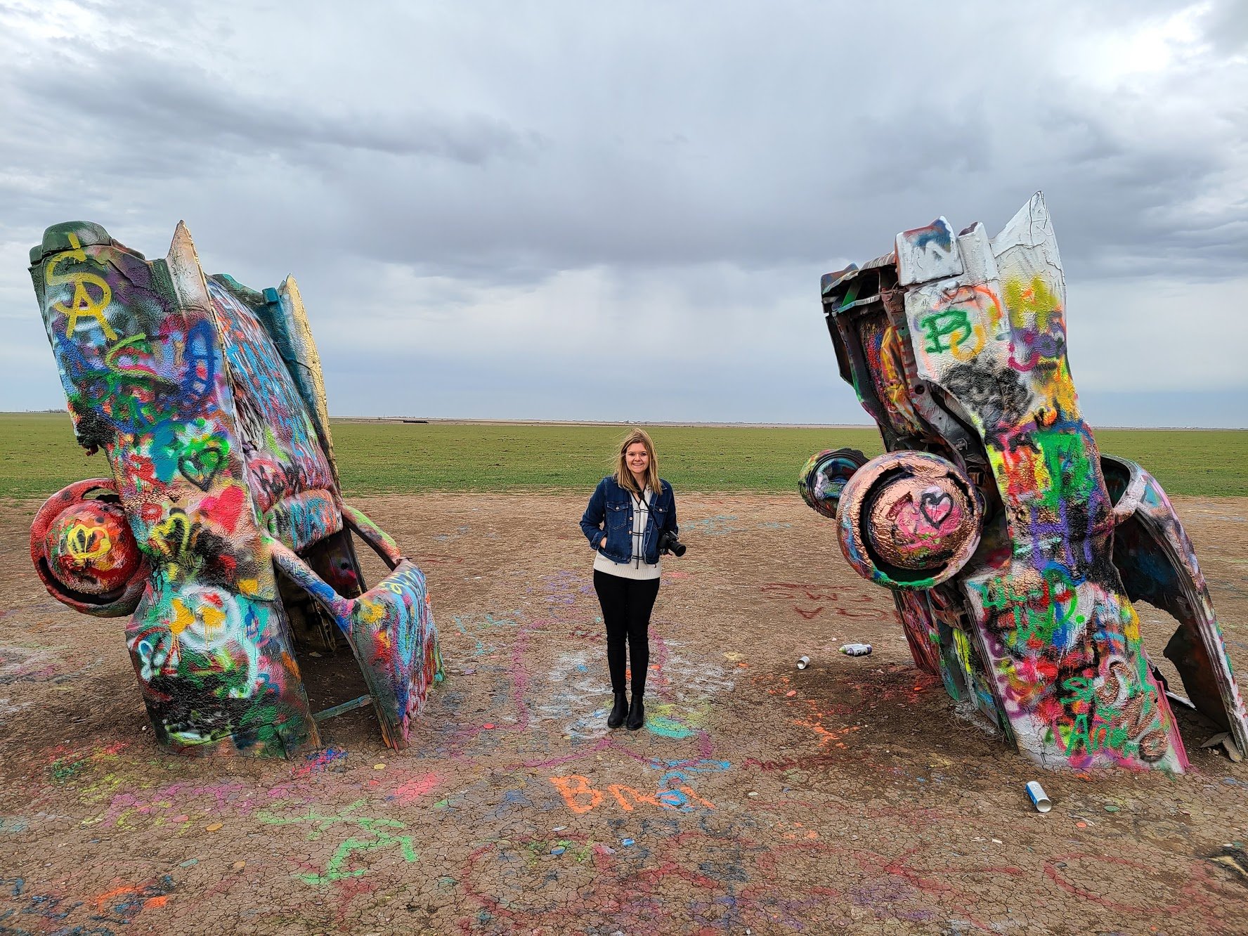 Lydia standing in between two painted Cadillacs.